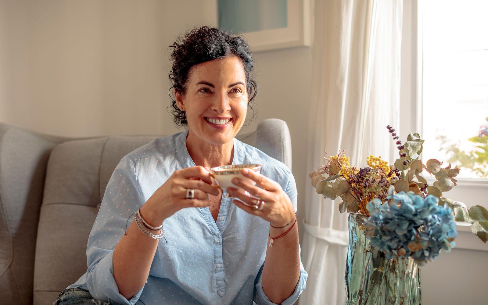Wechseljahre Symptome: Eine ältere Frau trinkt lächelnd eine Tasse Tee