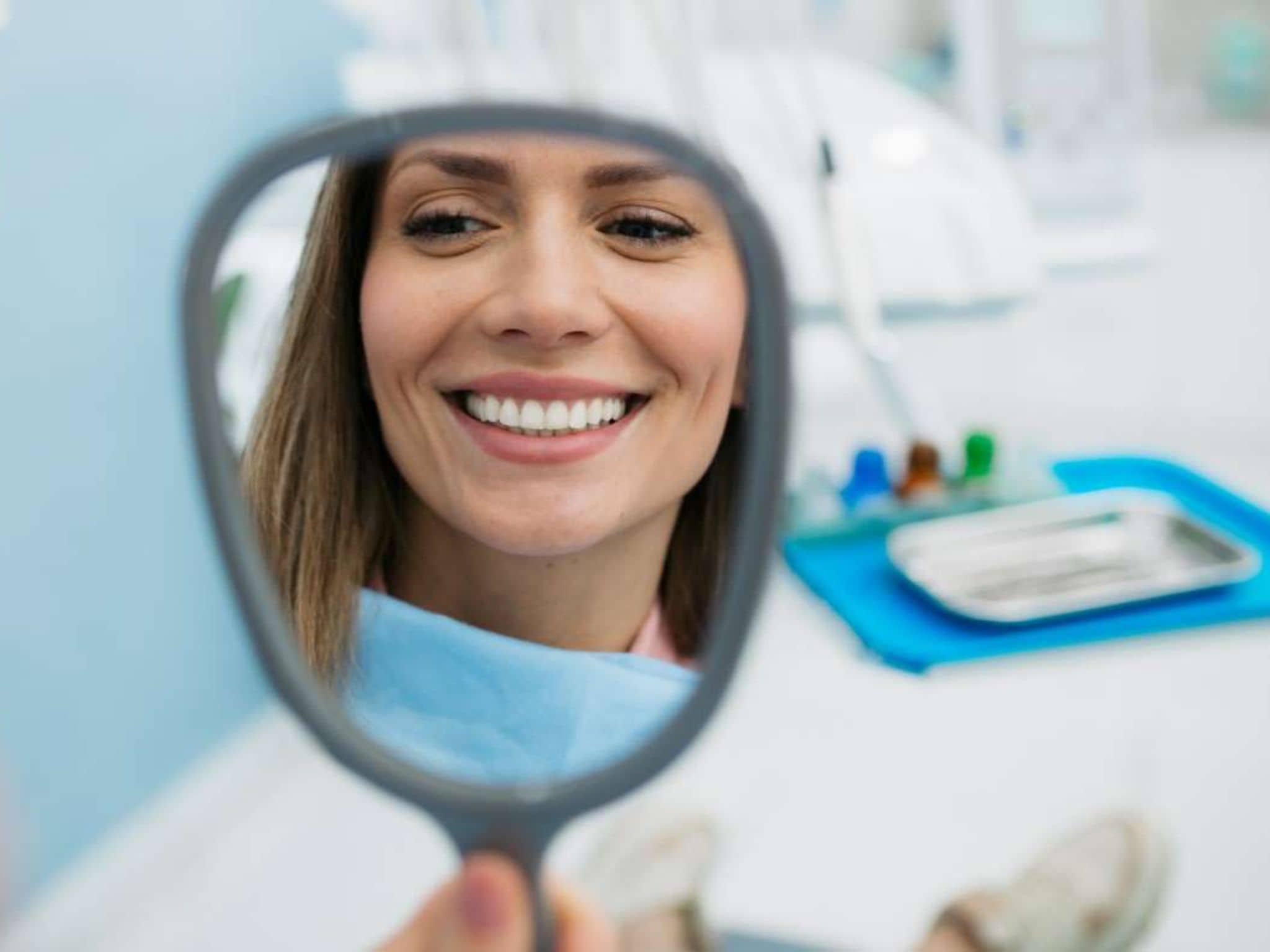 Professionelle Zahnreinigung: Junge Frau schaut sich nach der Behandlung ihre Zähne im Spiegel an.