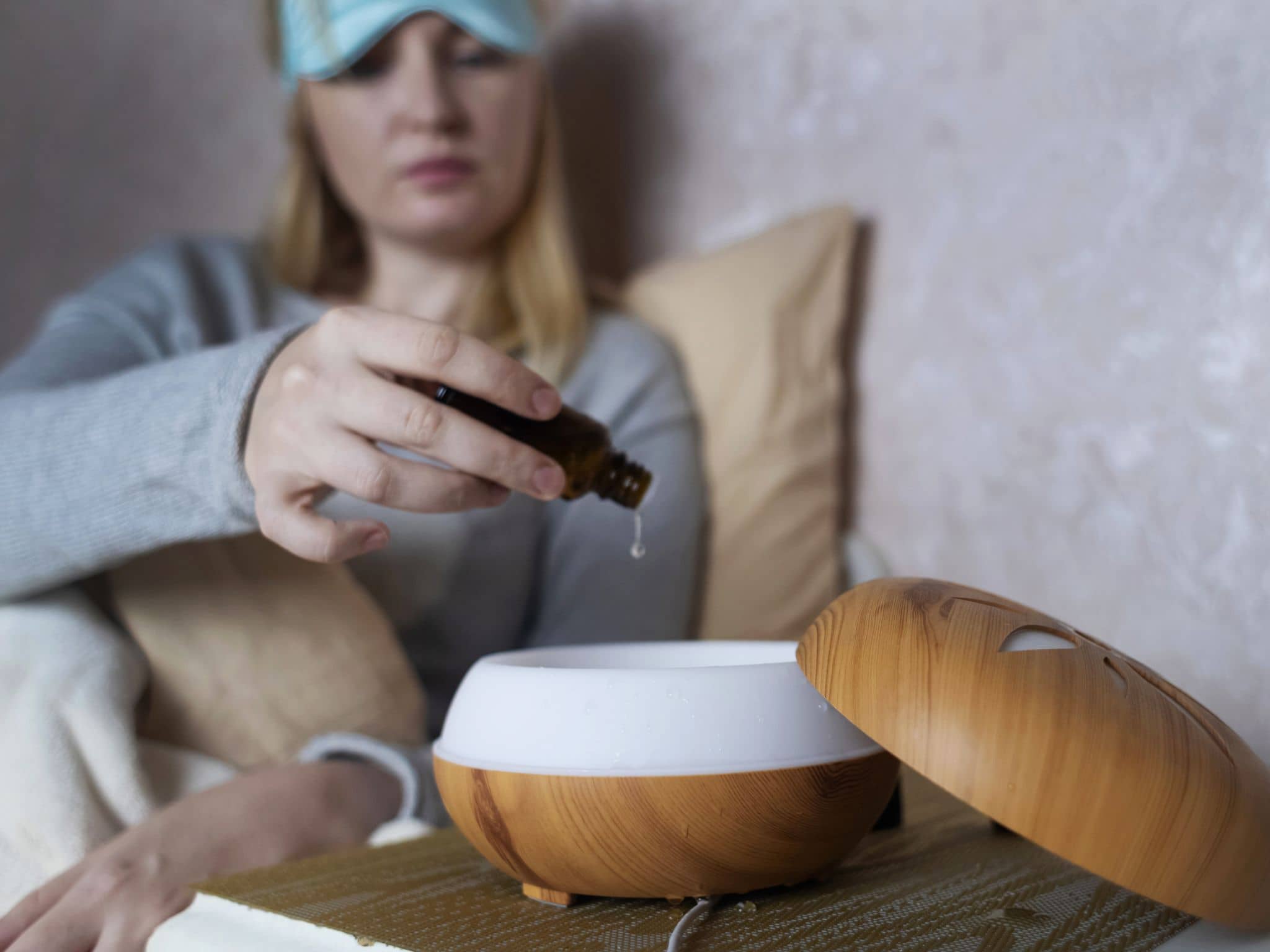 Raumduft Schlafzimmer: Eine Frau sitzt auf einem Bett und gibt Öl in einen Defuser