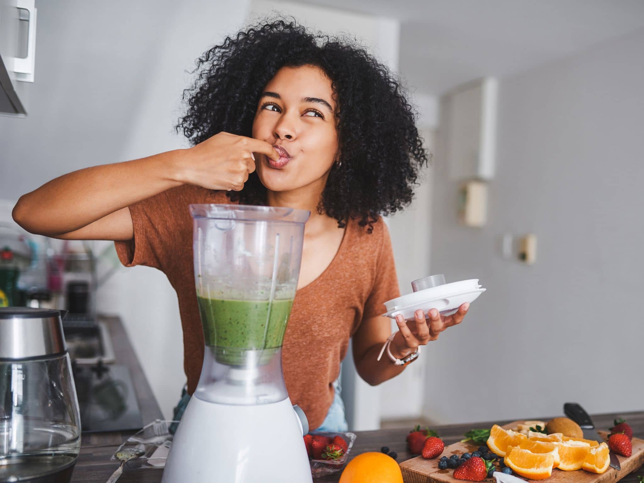 Eine junge Frau leckt den gesunden, frisch zubereiteten Smoothie von ihrem Finger ab.