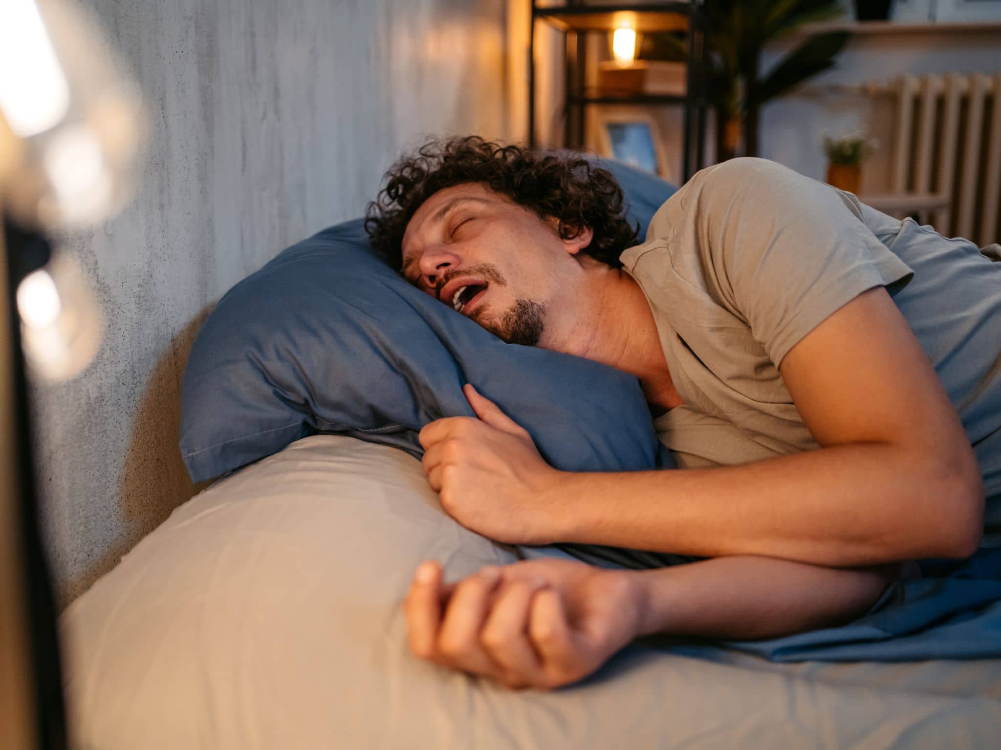 Ein Mann schläft mit weit geöffnetem Mund im Bett und scheint zu schnarchen.