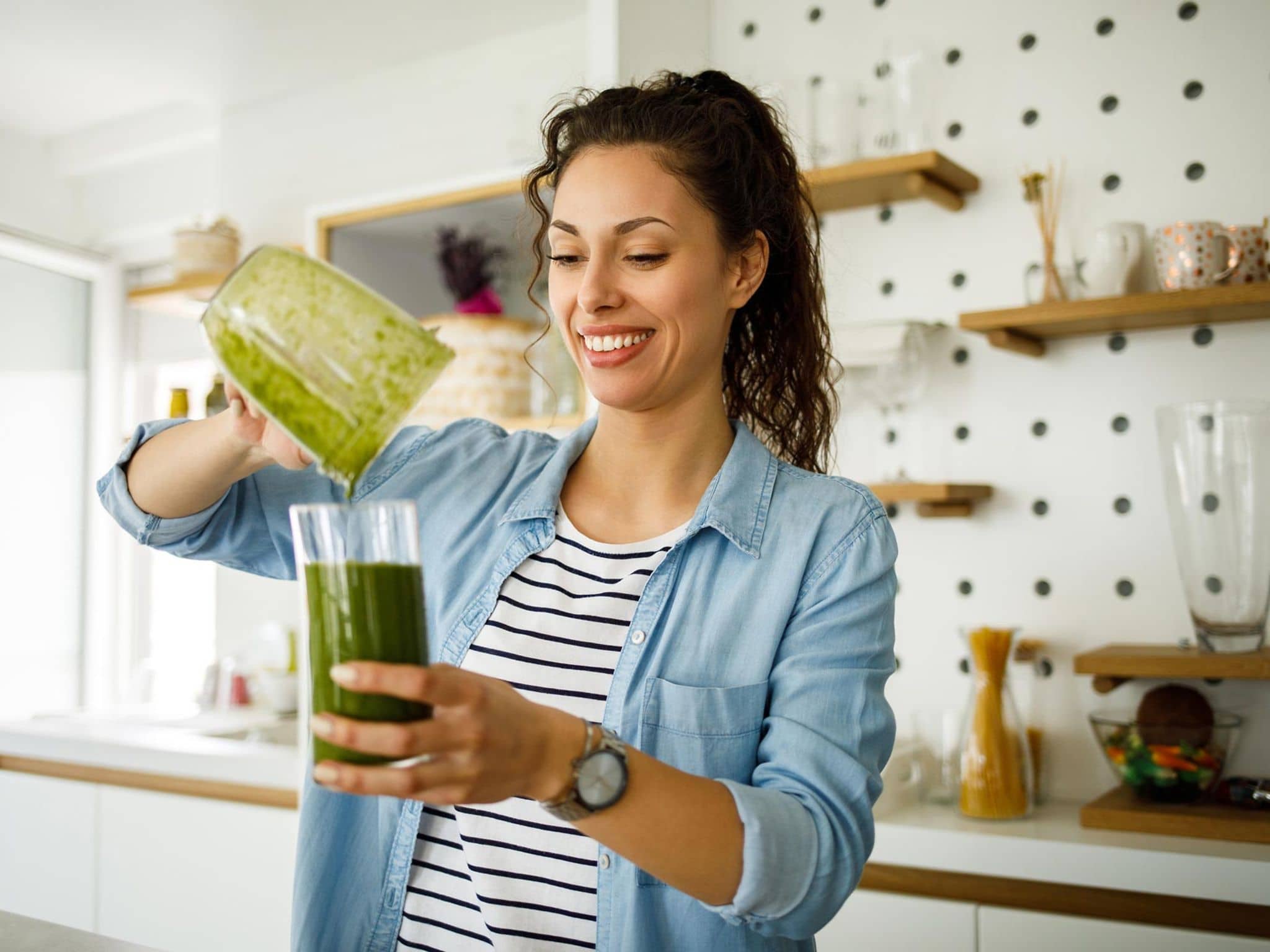 Gesunder Grünkohl: Junge Frau bereitet sich in ihrer Küche einen Grünkohl-Smoothie zu.
