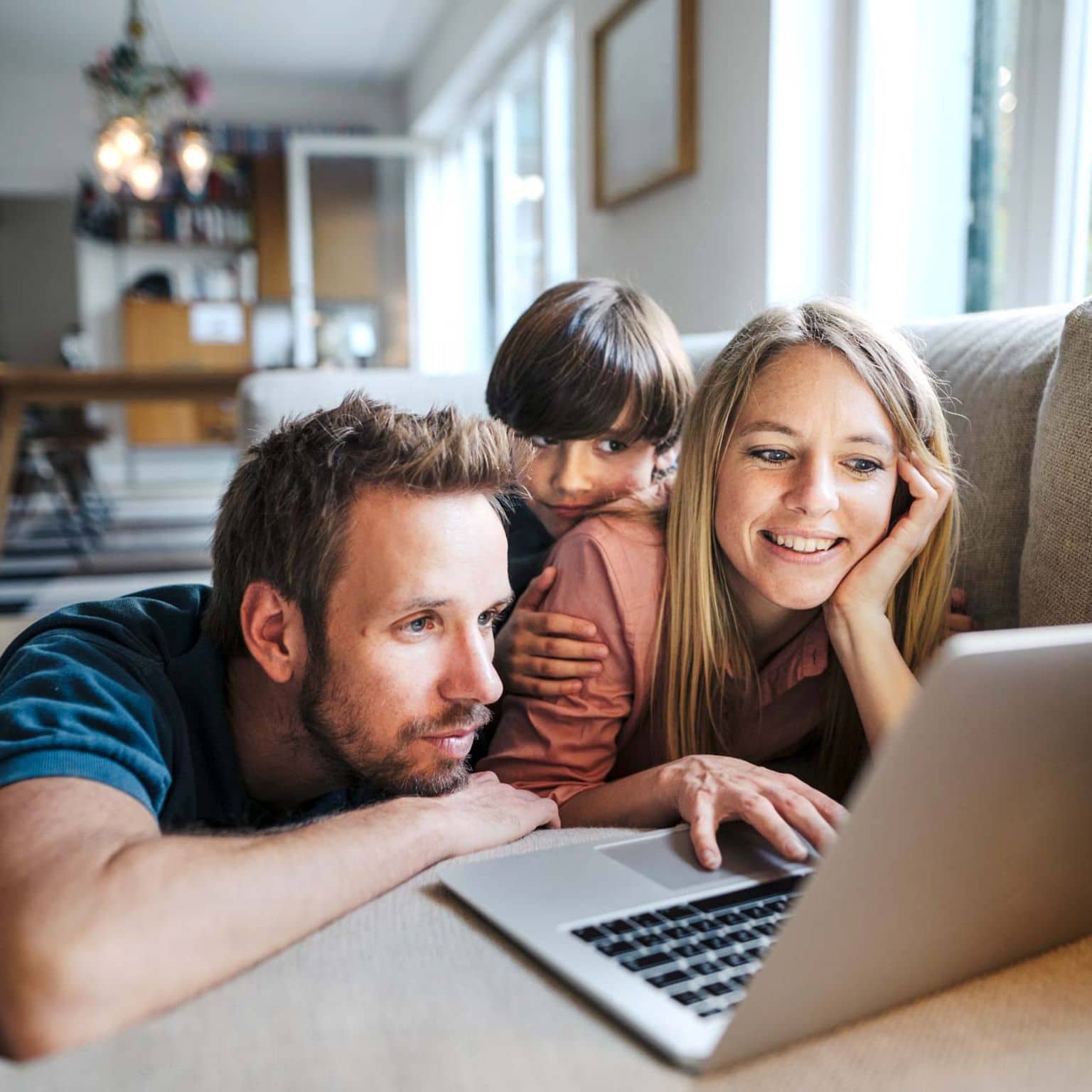 Vater, Mutter und Kind sitzen auf dem Sofa und schauen gemeinsam auf ein Notebook.