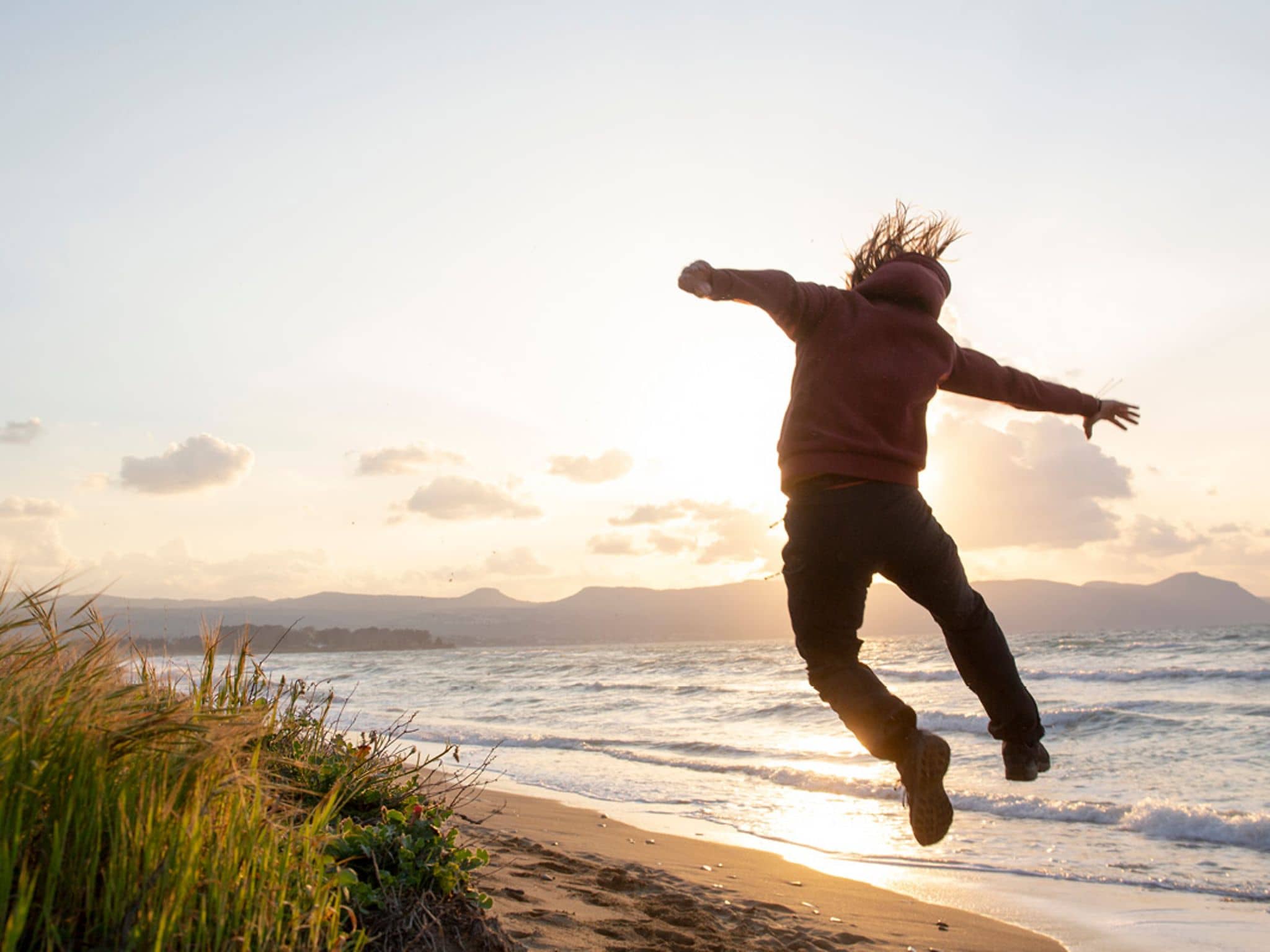 Ein Mann springt am Strand hoch und zeigt, dass er fit und vital ist.