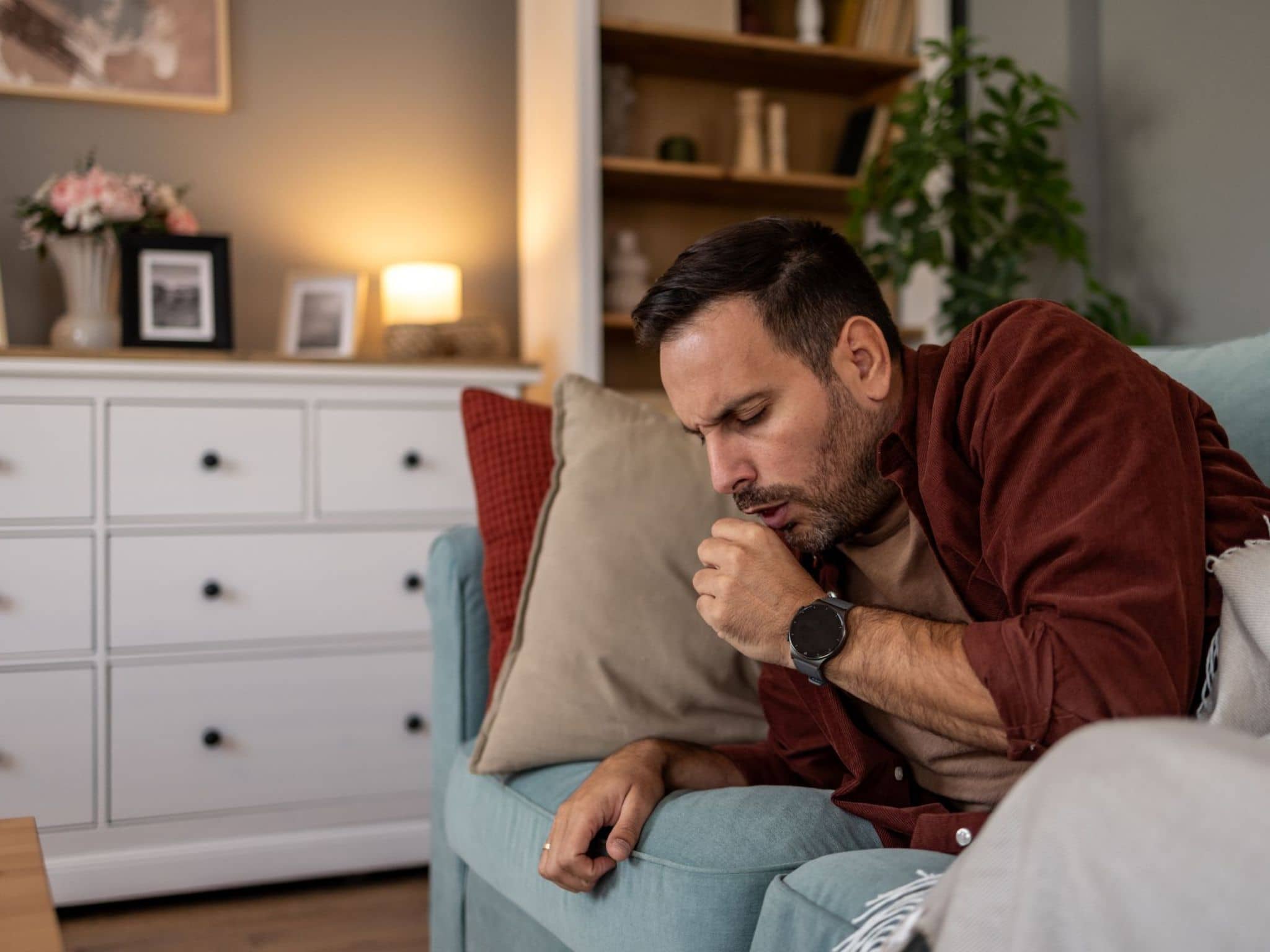 Ein kranker Mann liegt auf dem Sofa und hustet.