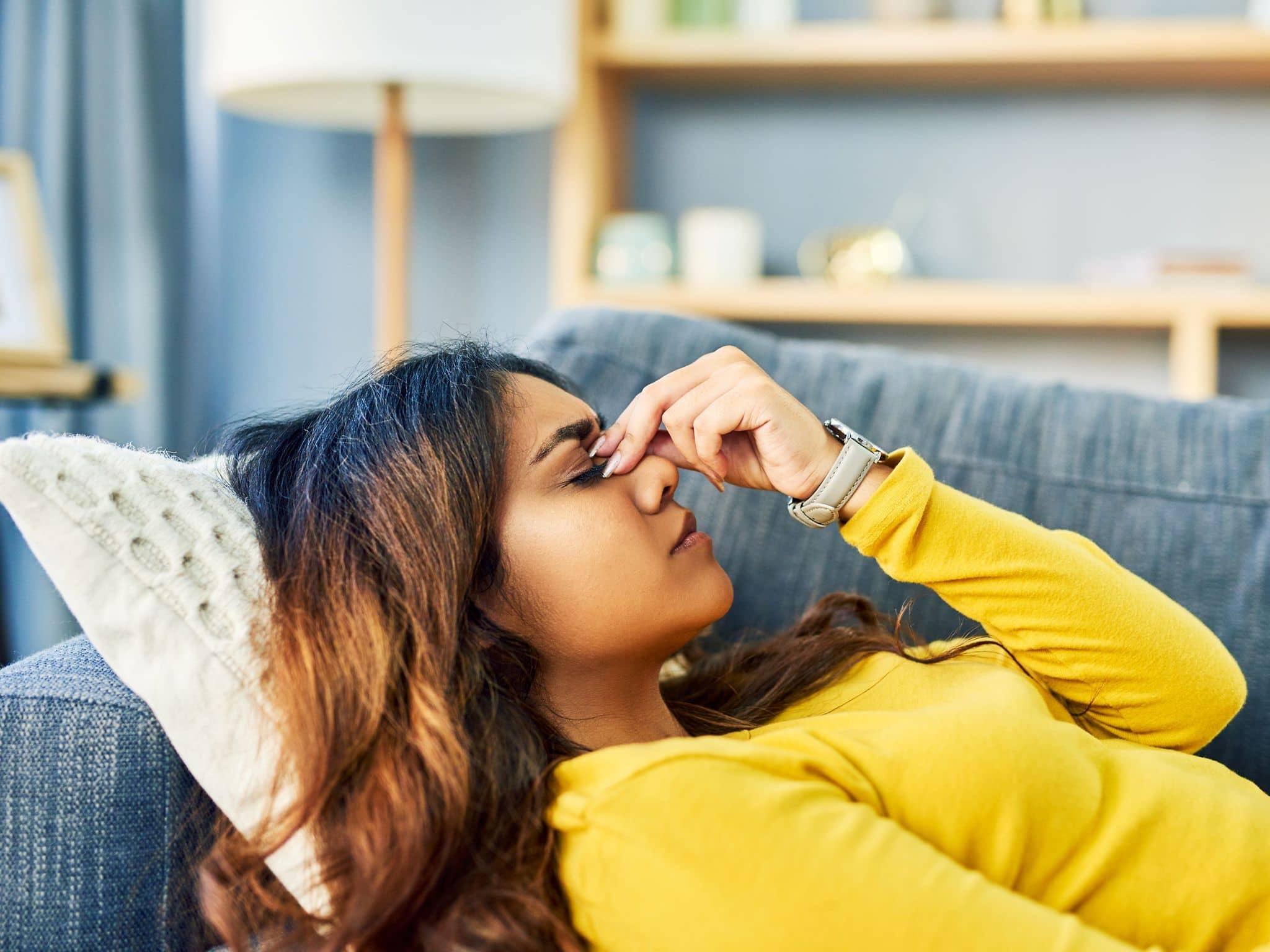 Eine Frau liegt auf dem Sofa und fasst sich an die Stirn, weil ihr schwindelig ist.