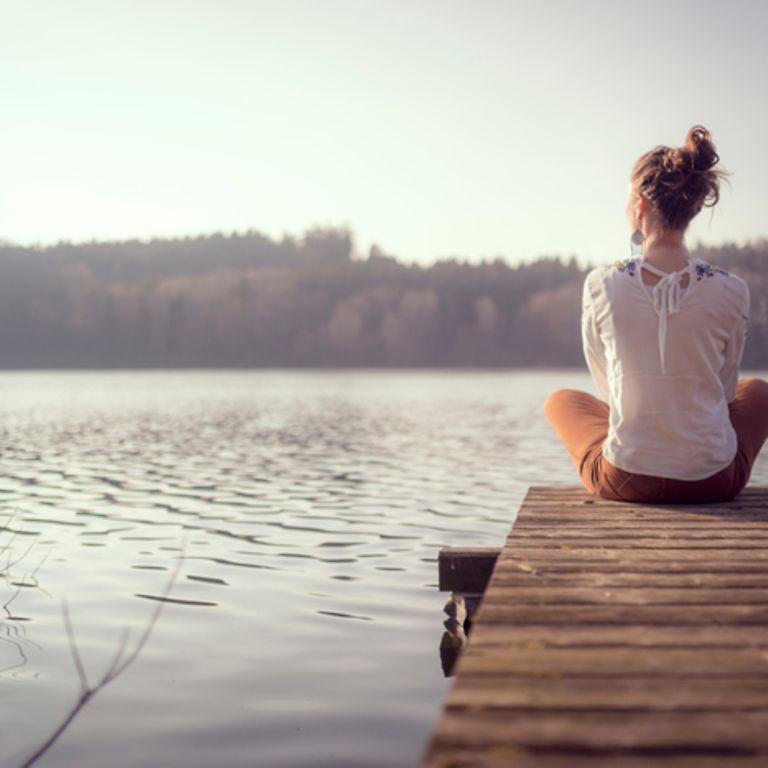 Frau sitzt an einem See auf Steg
