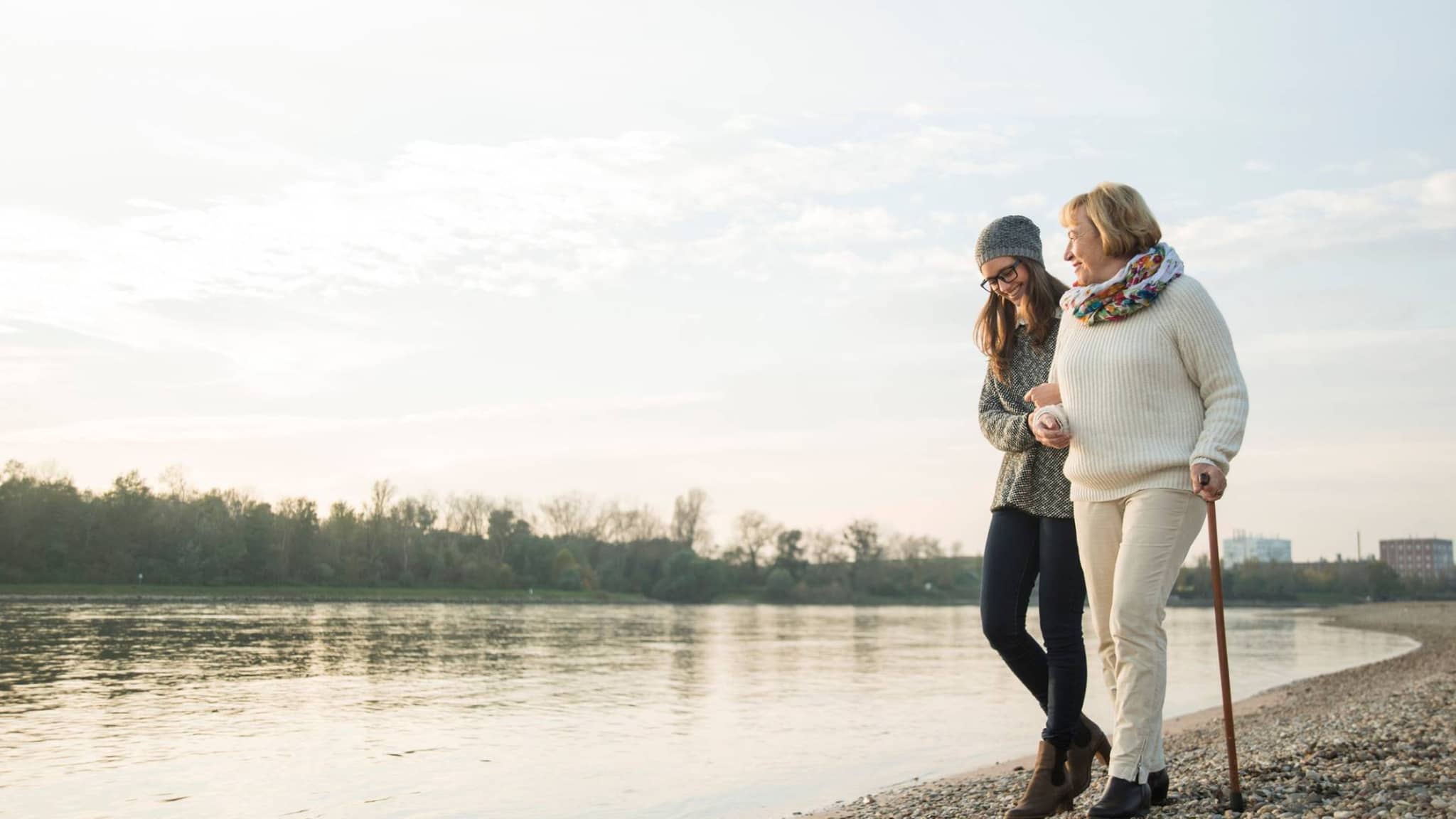 Pflege: Junge Frau spaziert mit ihrer Großmutter am Fluß entlang.