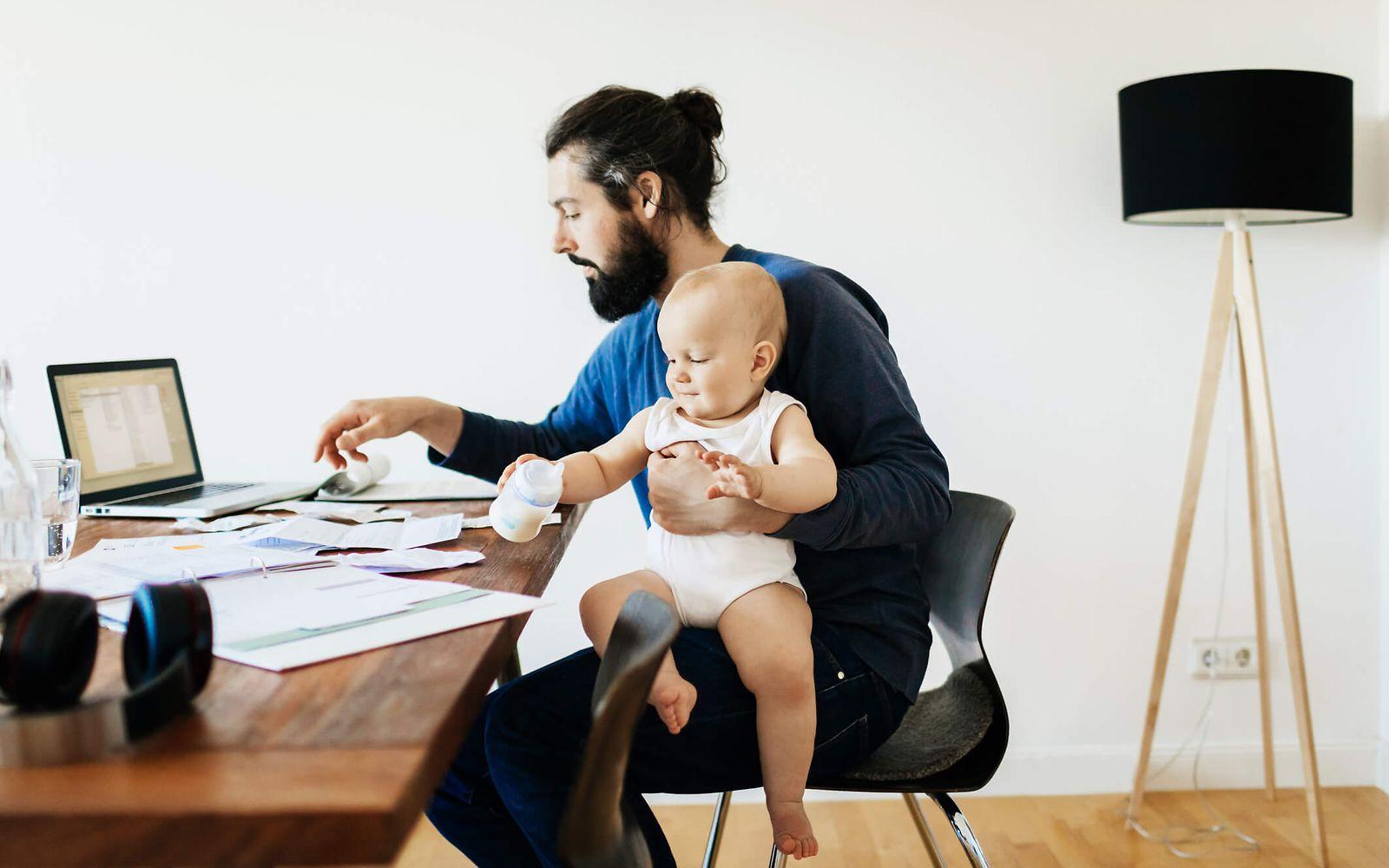 Bild: Vater sitzt am Schreibtisch und hat ein Kleinkind auf dem Schoß.