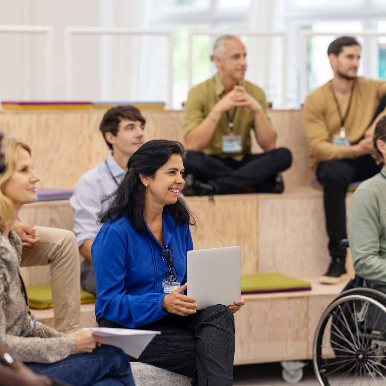 Bild: Personen sitzen auf einer kleinen Tribüne bei einer Veranstaltung und hören aufmerksam zu.