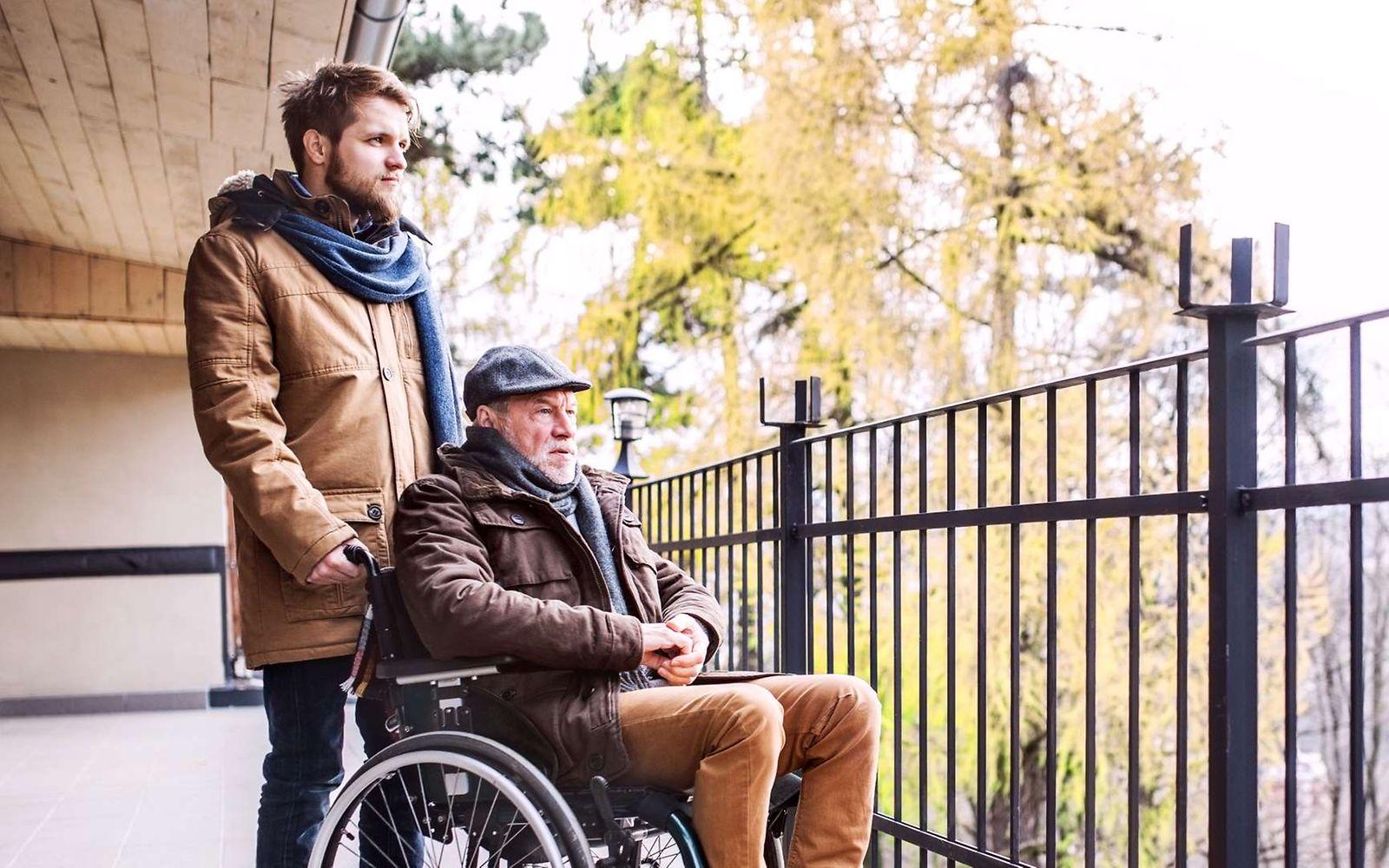 DAK-Pflegereport 2024: Älterer Mann im Rollstuhl schaut zusammen mit einem Pflegenden von einem Balkon aus in die Natur.