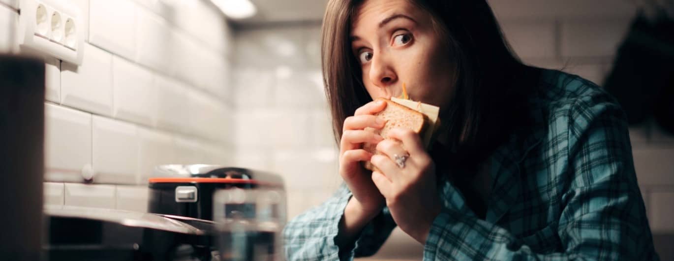 Eine Frau hat eine Heißhungeratacke und beißt in ein Käsebrot.