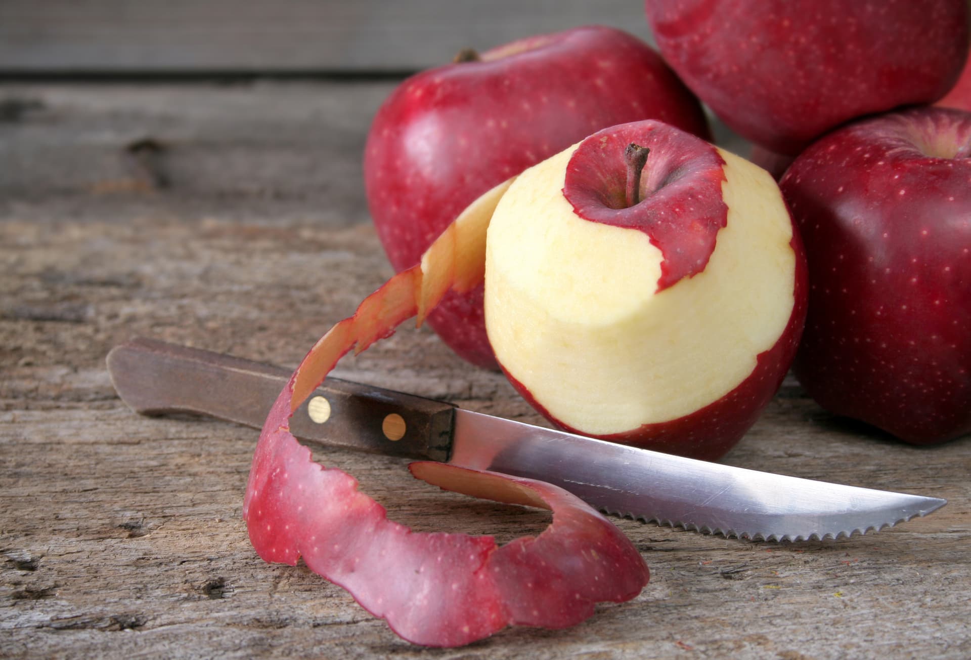Roter Apfel etwas geschält mit scharfem Messer daneben