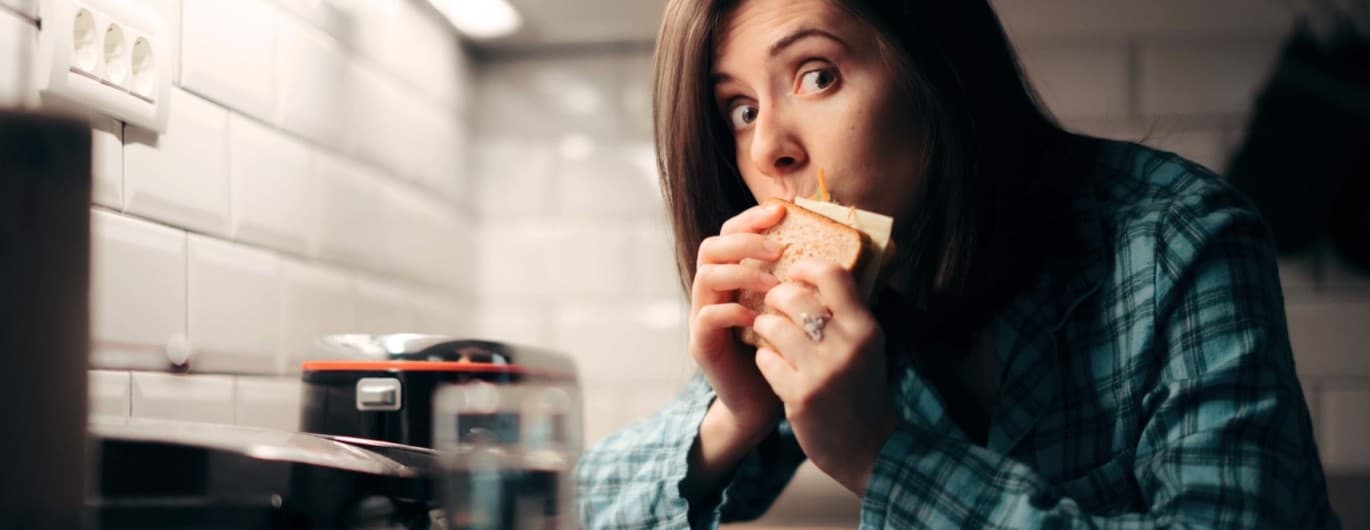 Eine Frau hat eine Heißhungeratacke und beißt in ein Käsebrot.