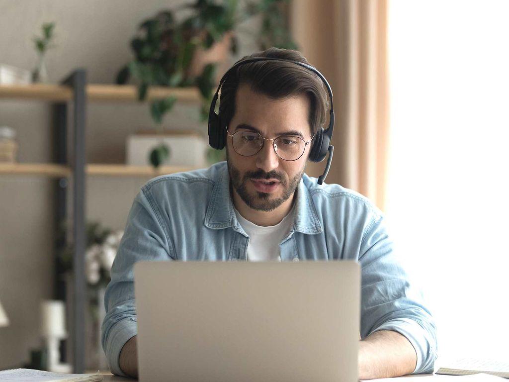 Bild: Mann mit Headset und Brille ist am Laptop in einem Gespräch.