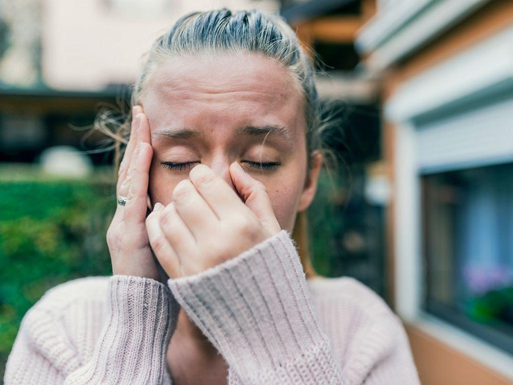 Spannungskopfschmerzen: Frau mit geschlossenen Augen hält die Hände an Schläfe und Nase.
