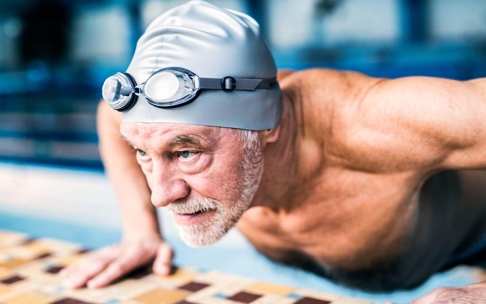 Prostatakrebsvorsorge: Älterer Mann mit Badekappe liegt auf dem Bauch am Schwimmbeckenrand.