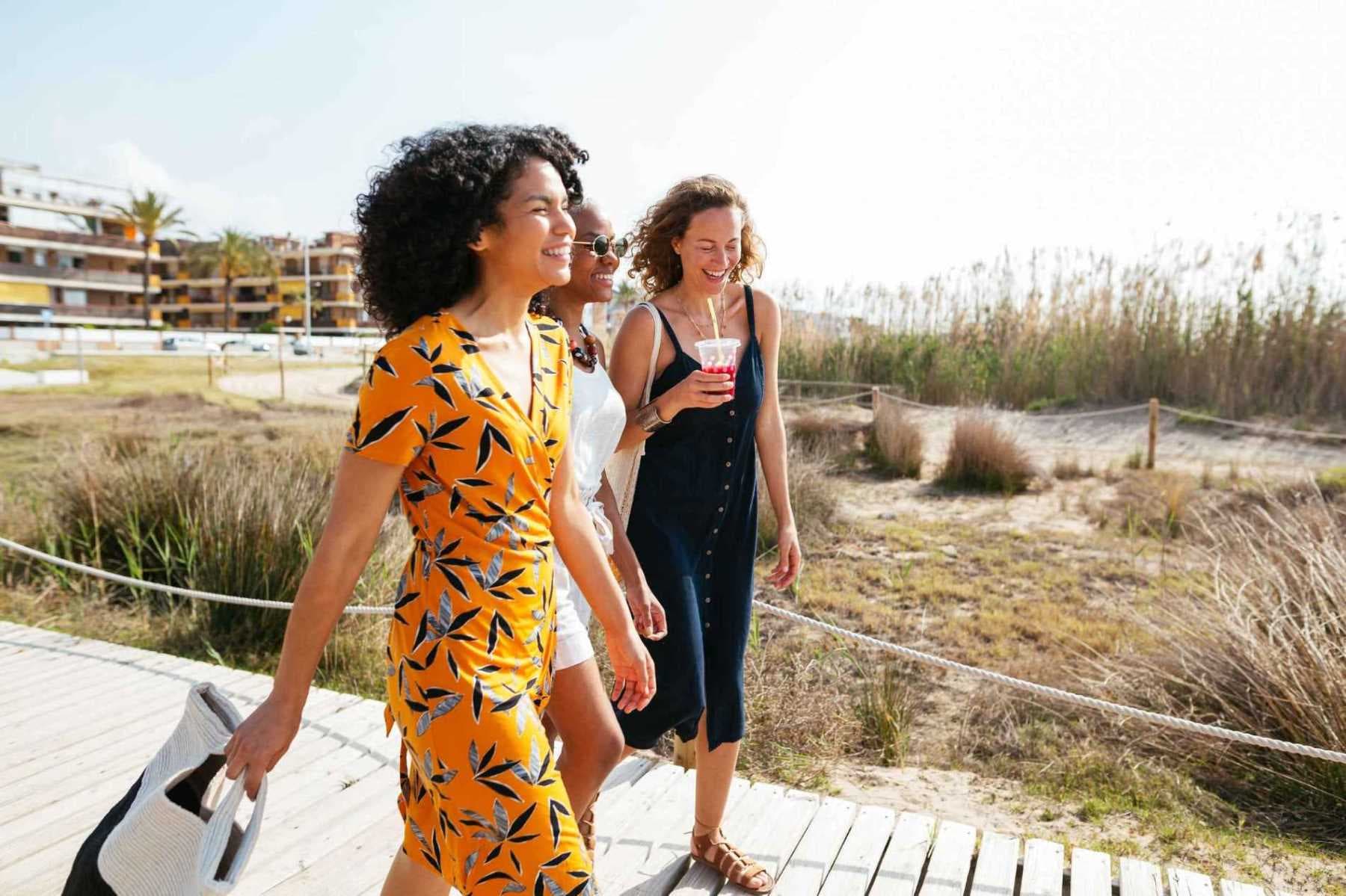 Brustkrebsvorsorge: Drei lachende Frauen in sommerlichen Kleidern gehen spazieren.