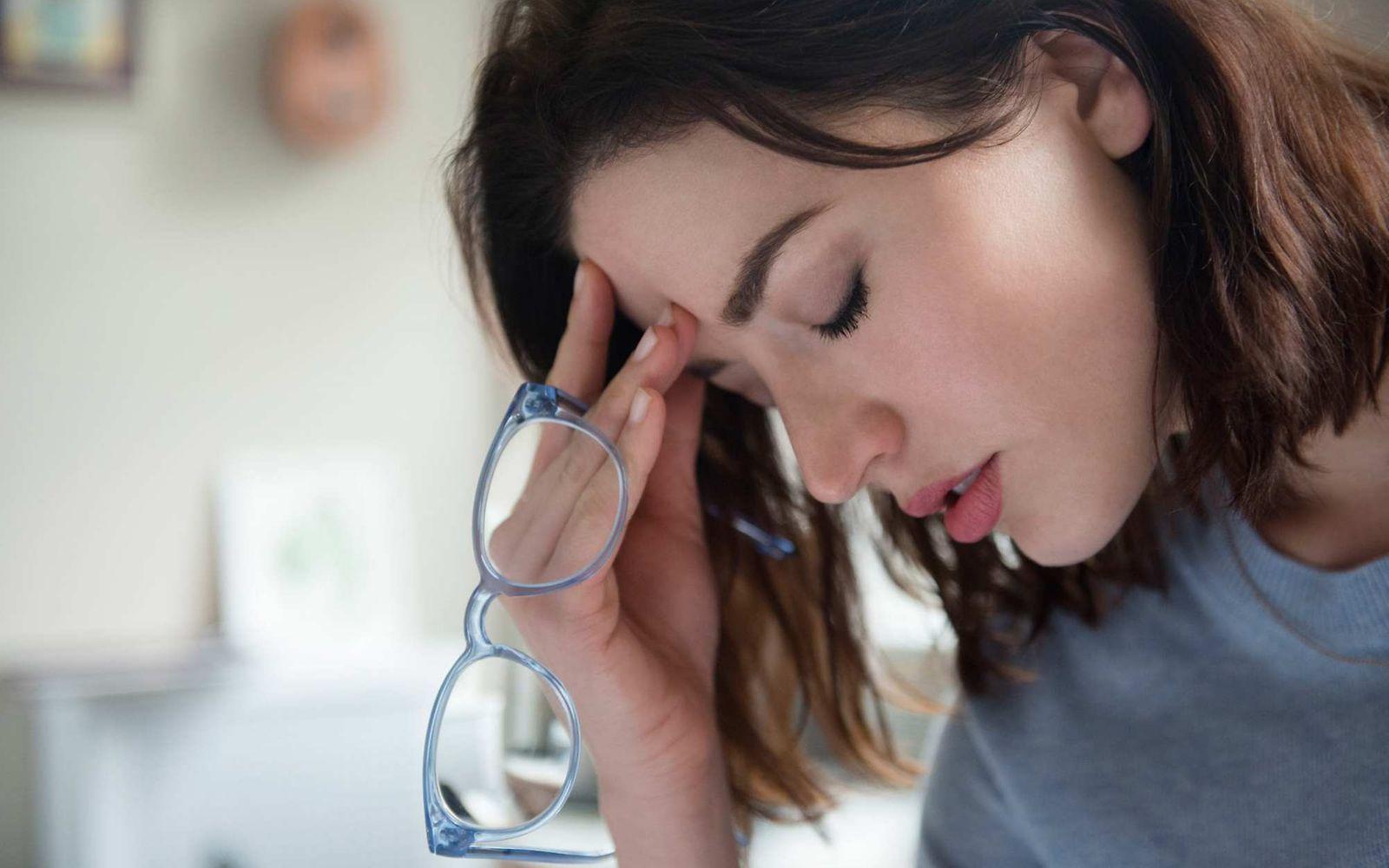 Clusterkopfschmerzen: Frau hält Brille in der Hand und fasst sich an die Stirn.