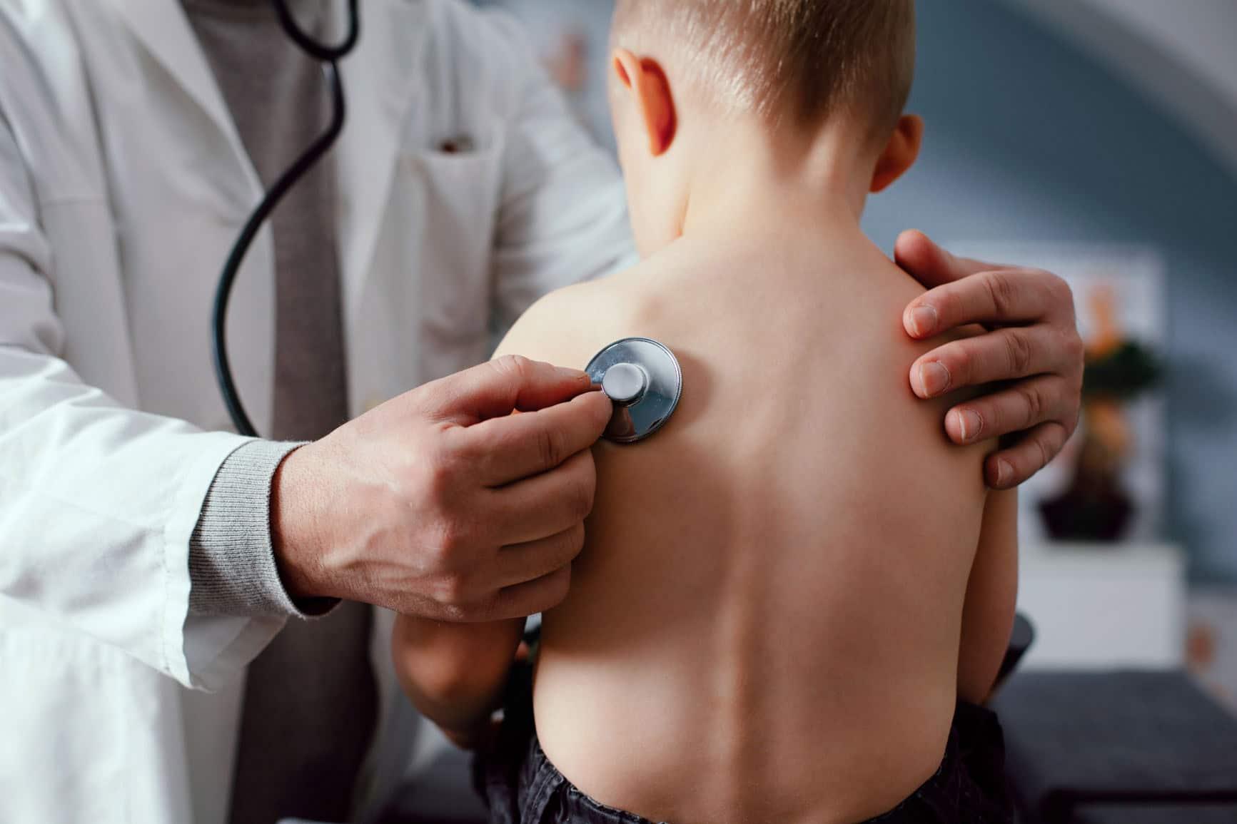 DMP Asthma bei Kindern: Arzt hört einen kleinen Jungen am Rücken ab.