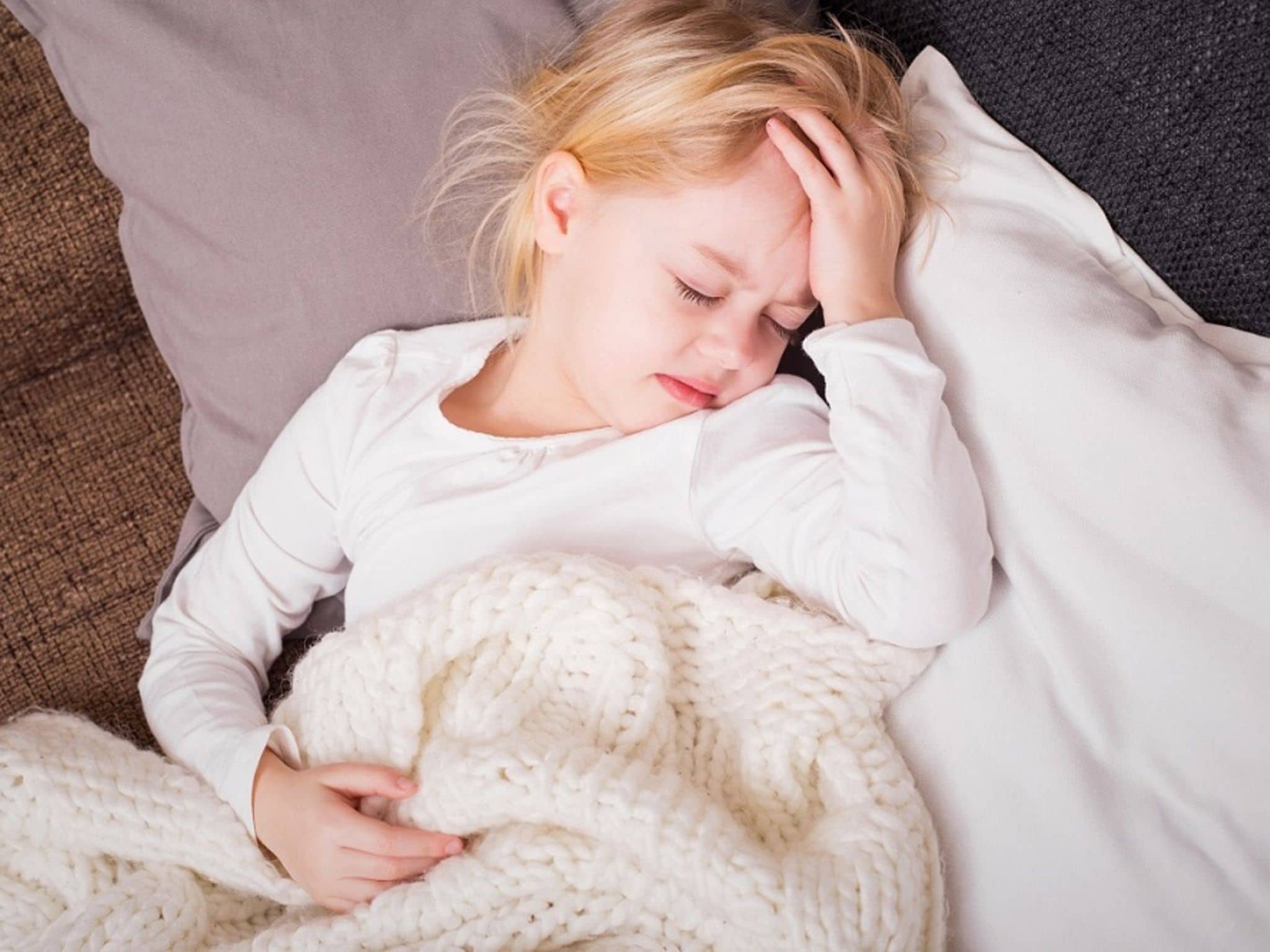 Kopfschmerzen bei Kindern: Kleines Mädchen hält mit schmerzverzerrtem Gesicht die Hand an den Kopf.