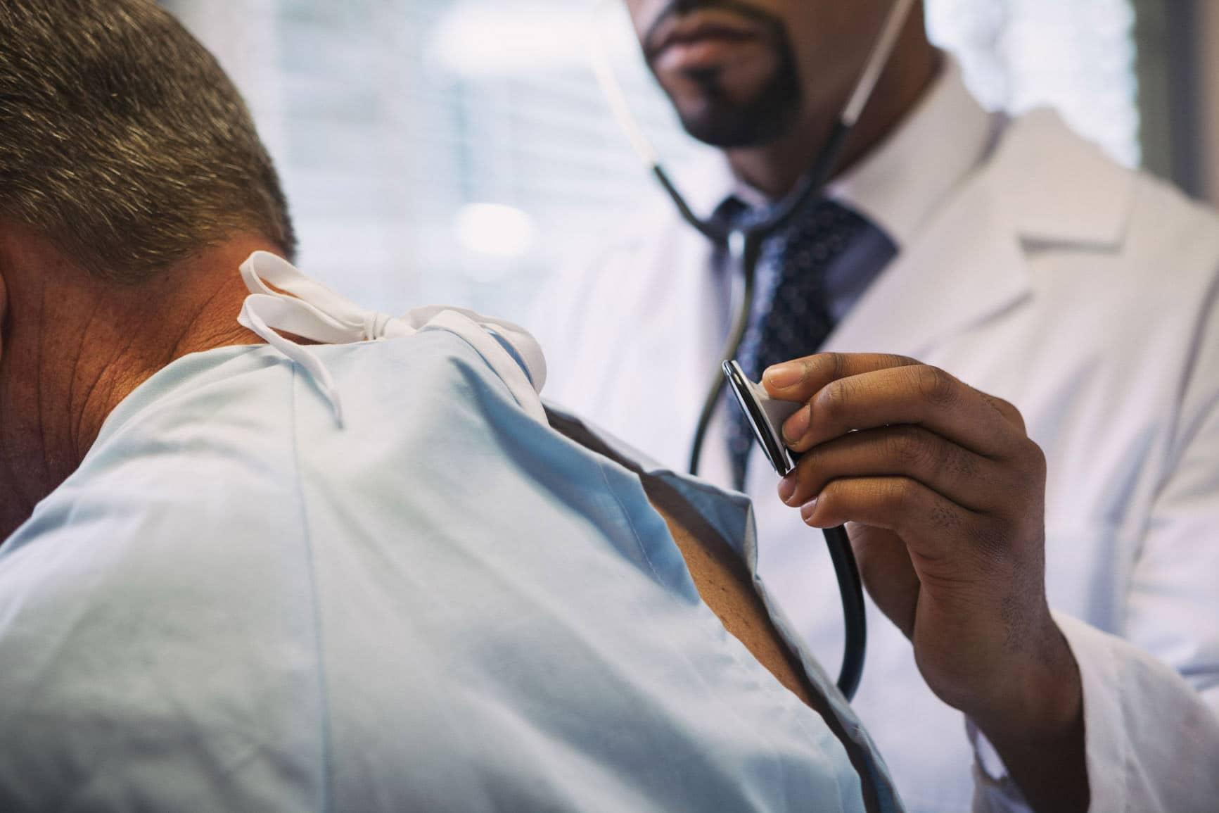 DMP COPD: Arzt hört den Rücken eines Mannes ab mit einem Stethoskop.
