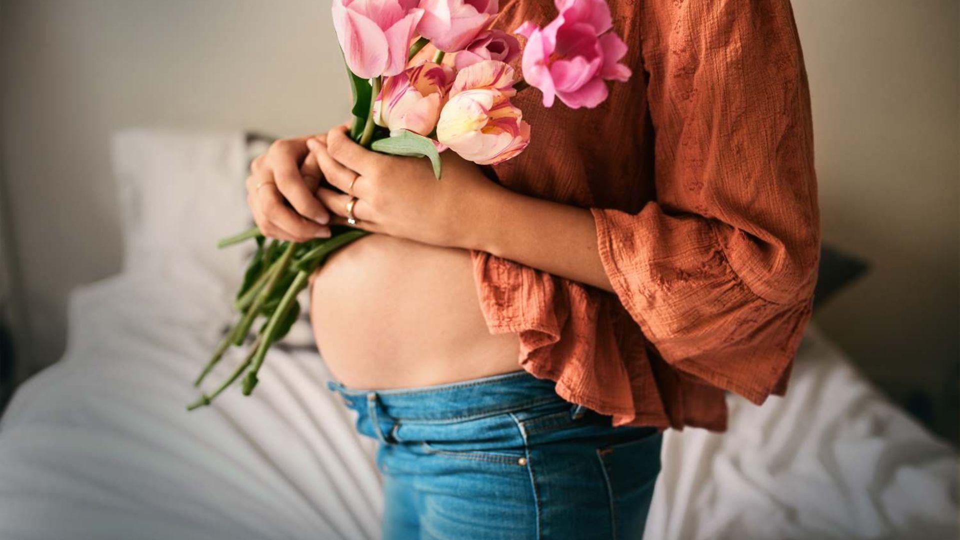 DAK MamaPLUS: Schwangere hält sich Blumen vor den nackten Bauch