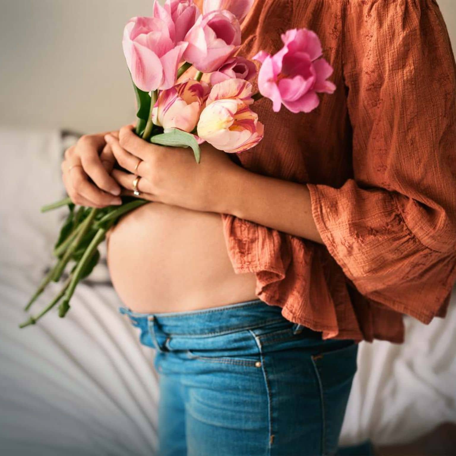 DAK MamaPLUS: Schwangere hält sich Blumen vor den nackten Bauch