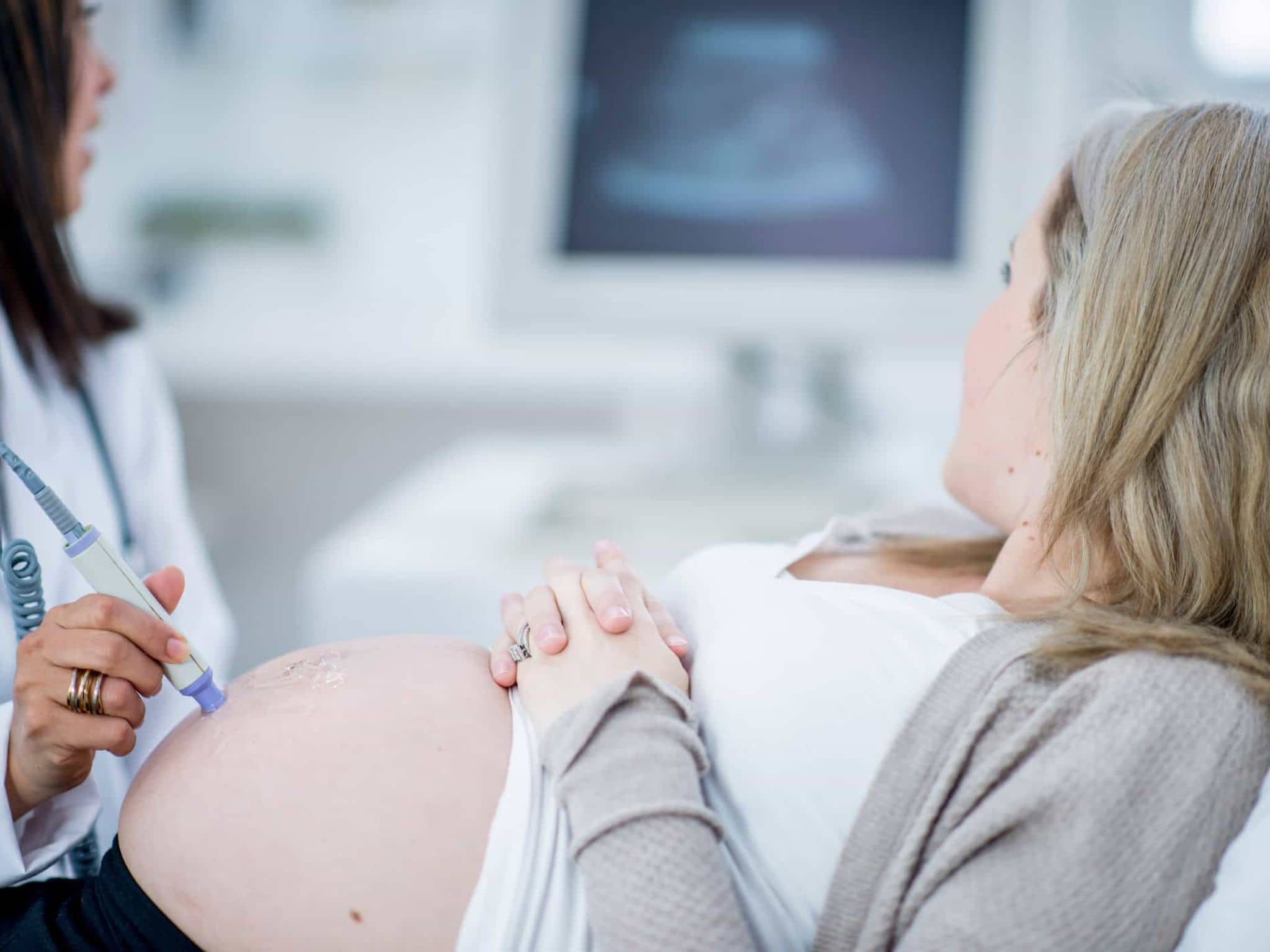 Vorsorgeuntersuchungen für Schwangere: Schwangere und Ärztin betrachten Monitor während einer Ultraschalluntersuchung.