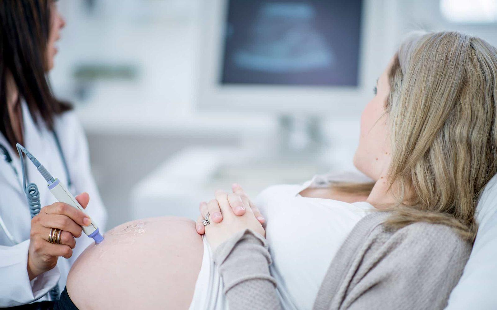 Vorsorgeuntersuchungen für Schwangere: Schwangere und Ärztin betrachten Monitor während einer Ultraschalluntersuchung.