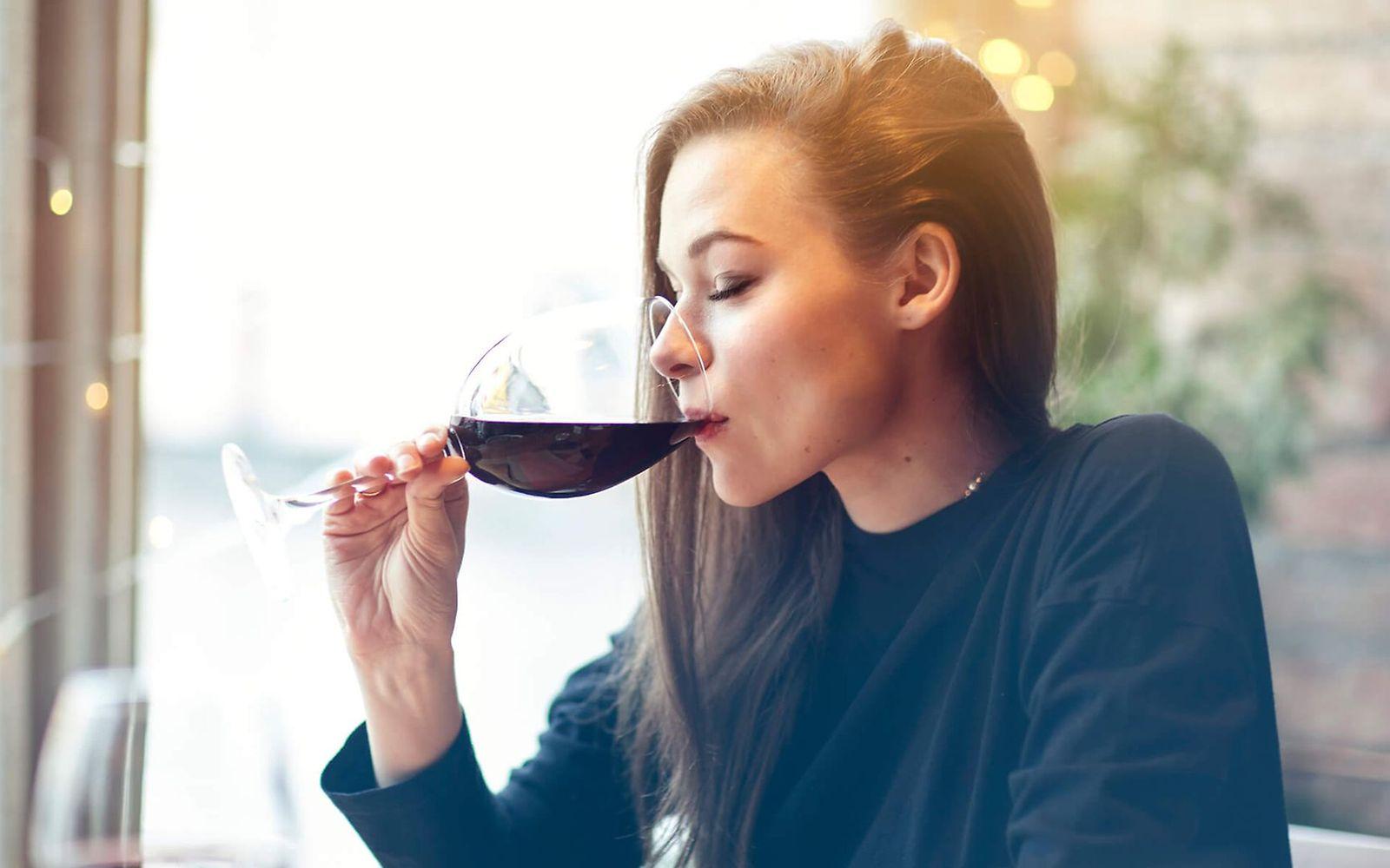 So wirkt Alkohol im Körper: Frau sitzt allein am Tisch und genießt ein Glas Rotwein