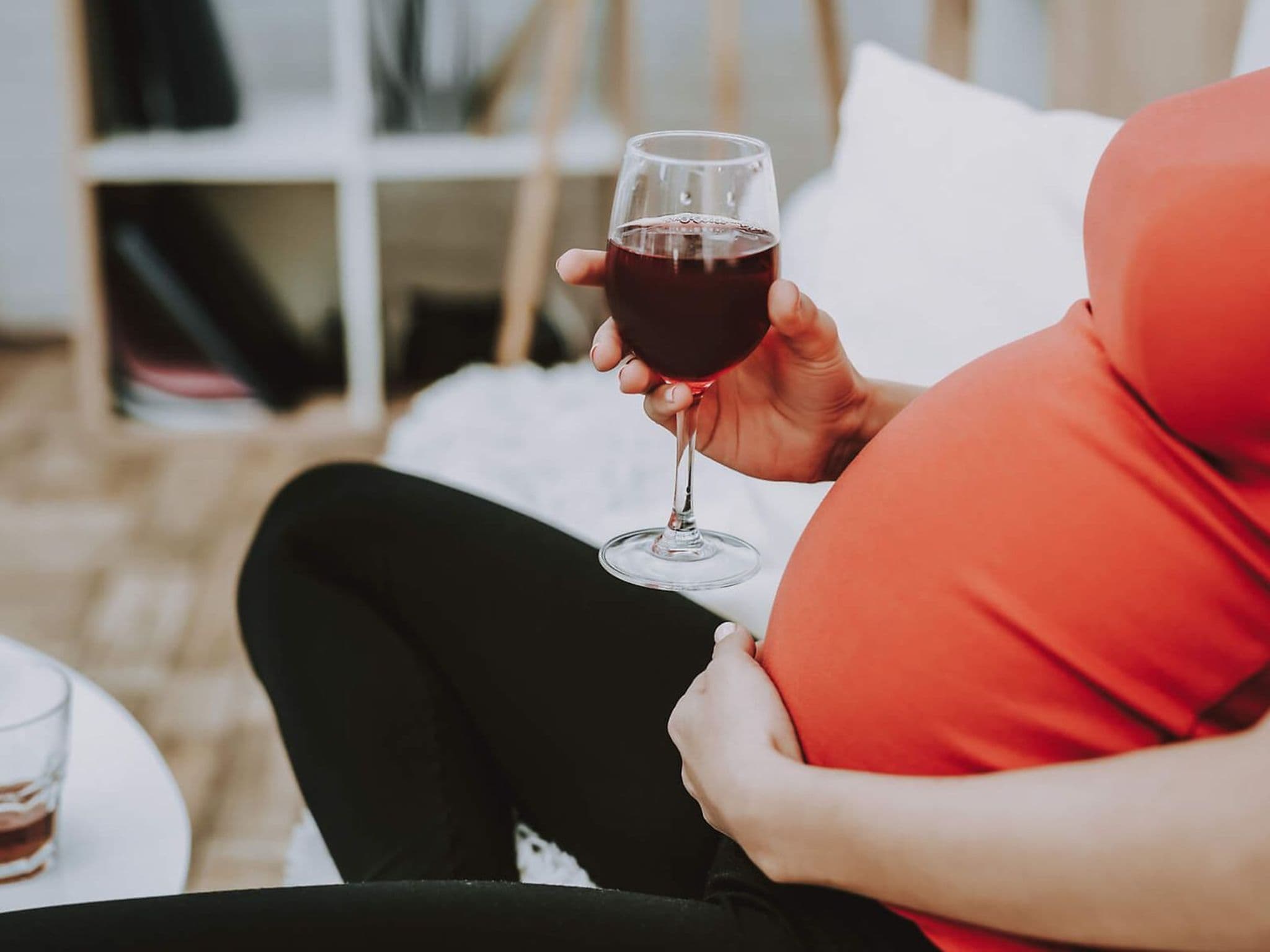 Alkohol in der Schwangerschaft: Schwangere sitzt vor einem Tisch mit Flaschen und Zigaretten und hält ein Glas Wein in der Hand