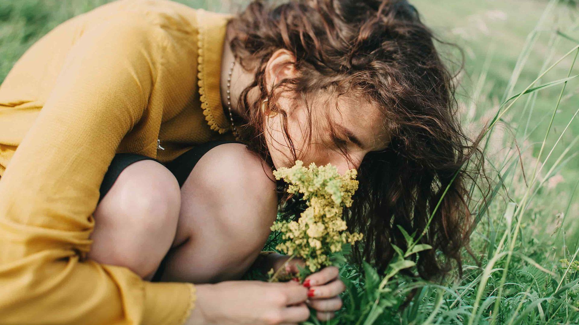 Allergien: Frau riecht an einer Blume auf einer Sommerwiese