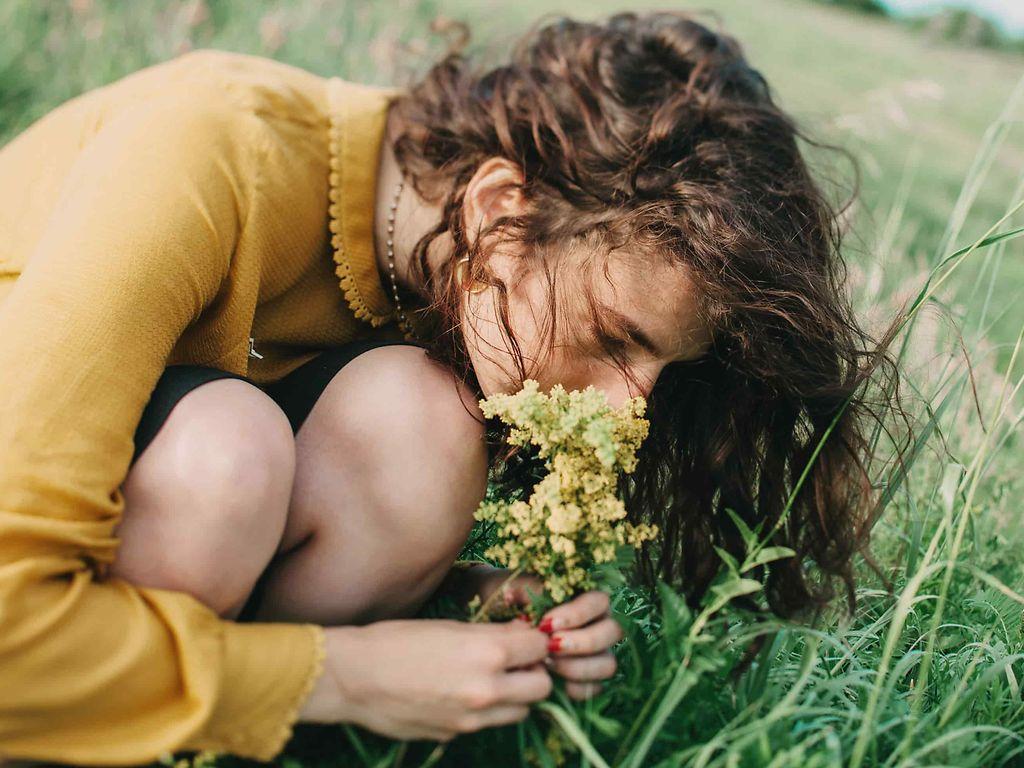 Allergien: Frau riecht an einer Blume auf einer Sommerwiese