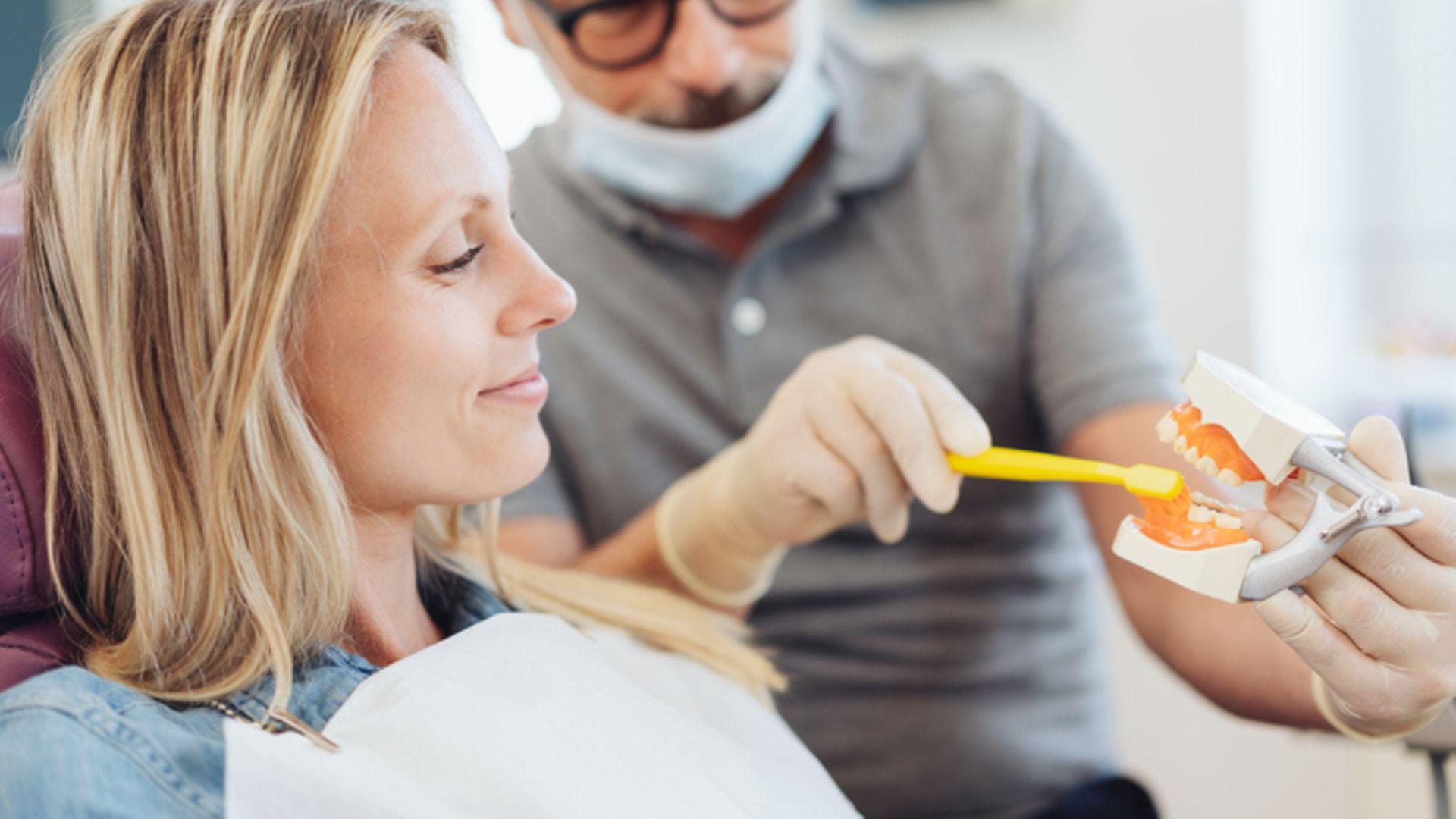 Was ist Parodontitis?: Zahnarzt erklärt Frau wie Zähne geputzt werden