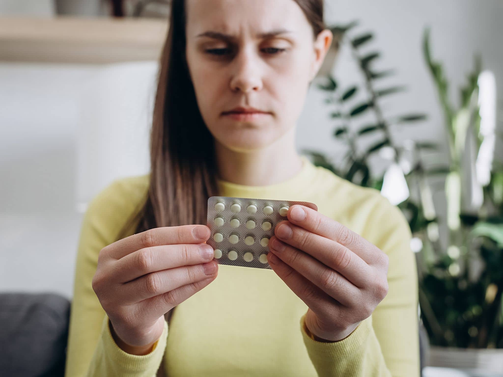 Medikamentensucht: Frau mit Augenringen blickt müde auf eine Packung Tabletten.