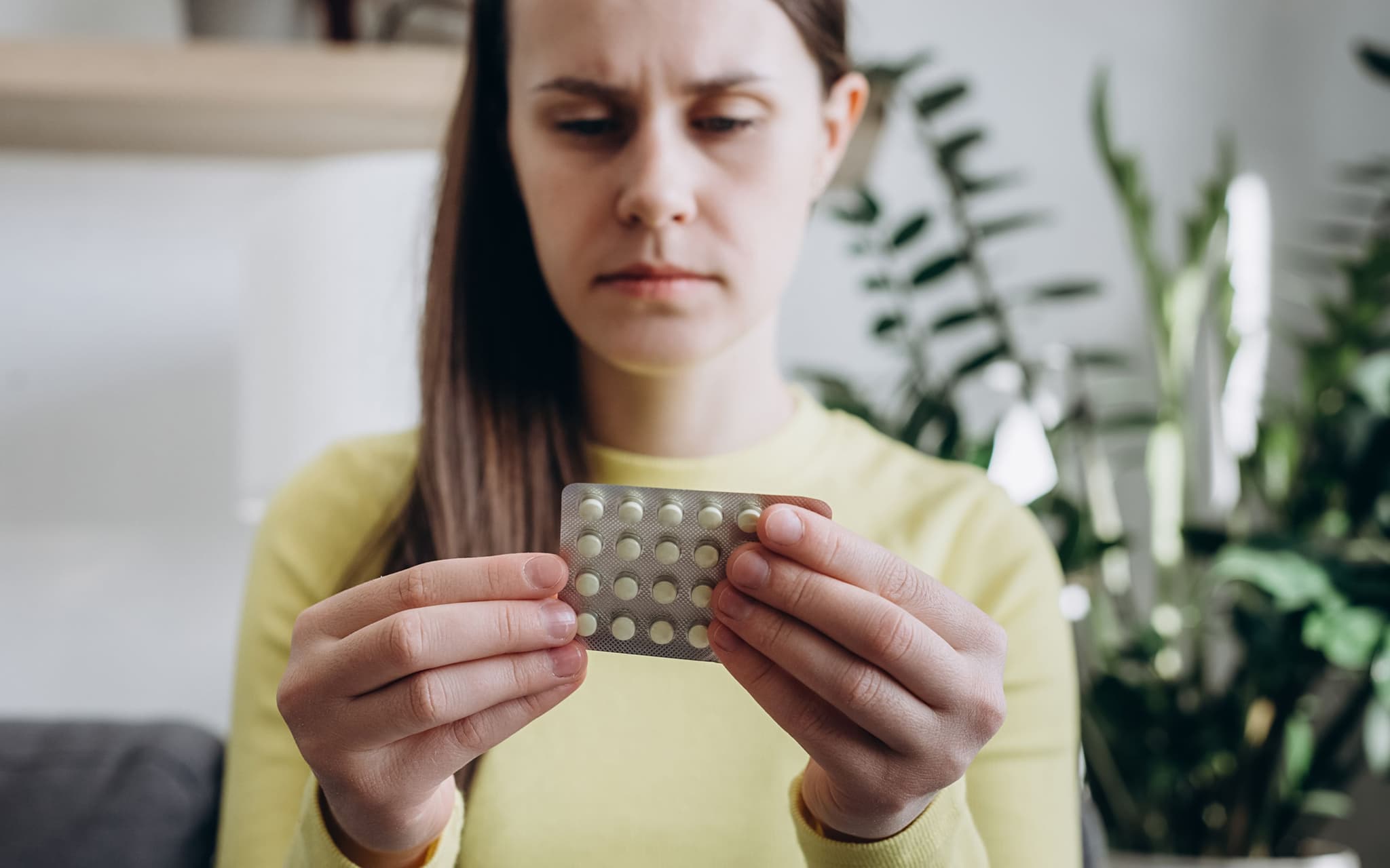 Medikamentensucht: Frau mit Augenringen blickt müde auf eine Packung Tabletten.