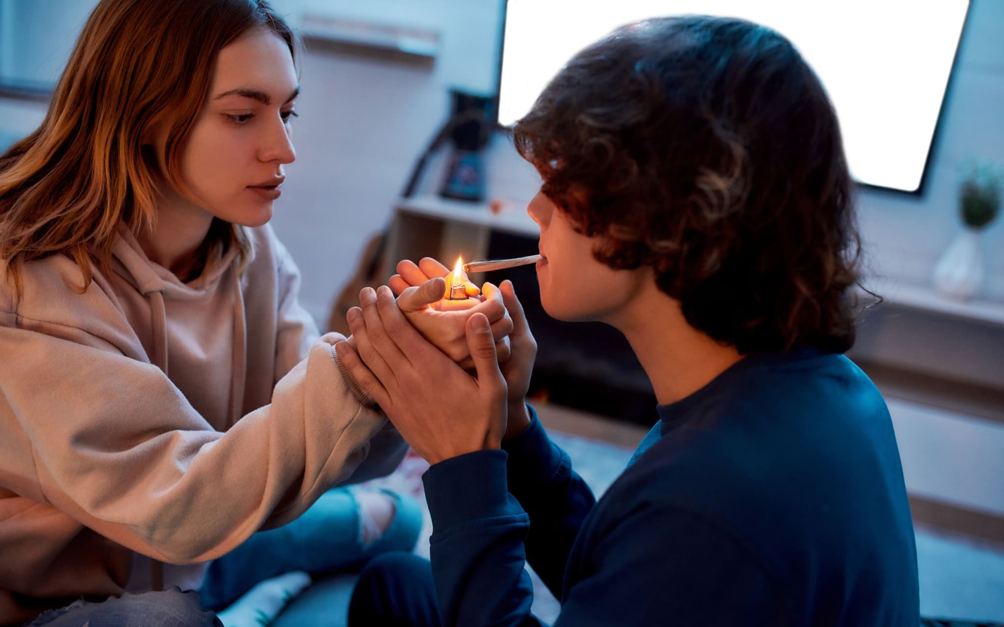 Cannabis: Junges Mädchen, das Cannabis-Zigarette für ihren Freund anzündet, während sie zu Hause auf der Couch sitzt.