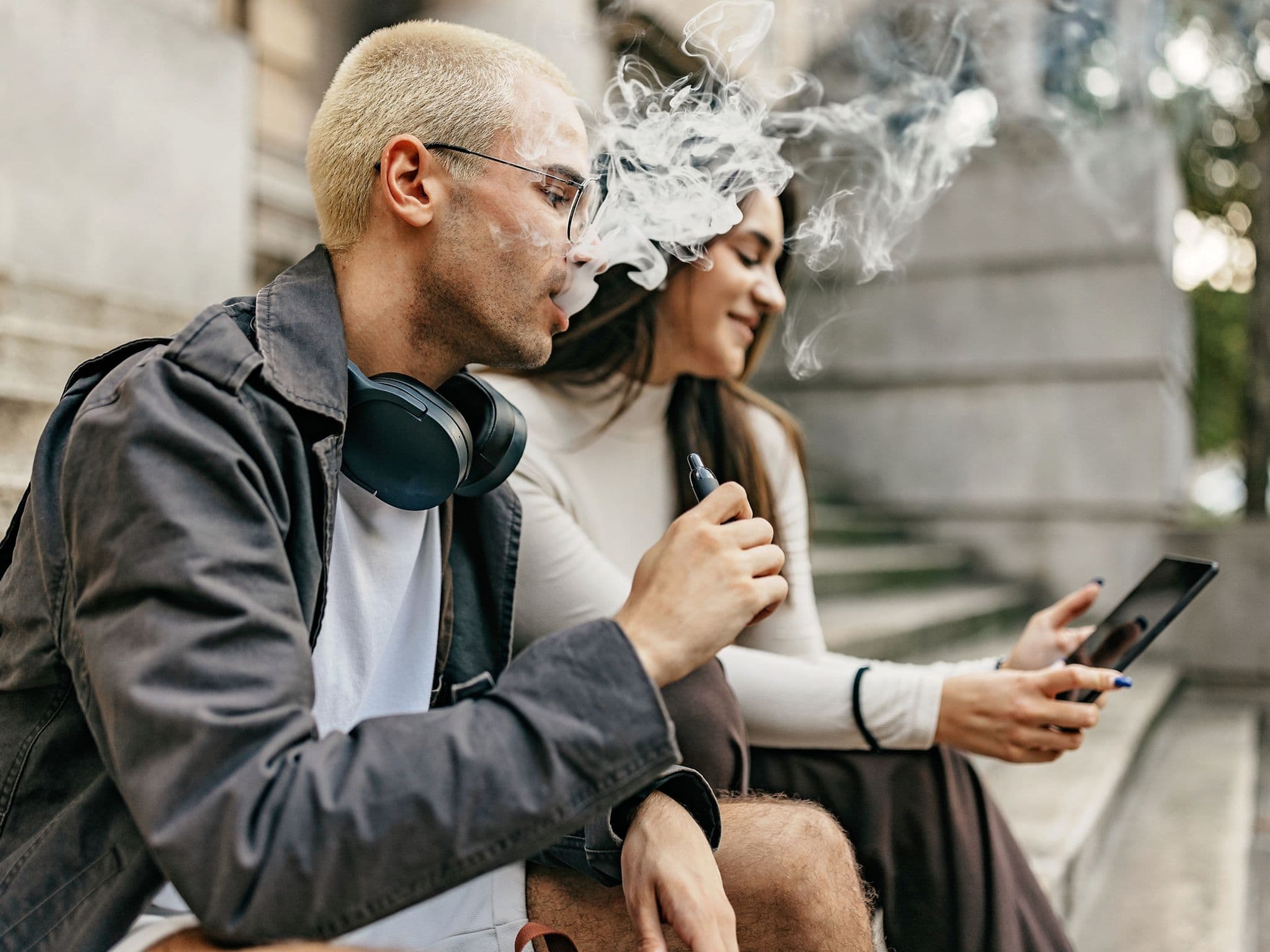 Vapen: Ein junger Mann und eine junge Frau sitzen auf einer Treppe, während der Mann eine E-Zigarette raucht.
