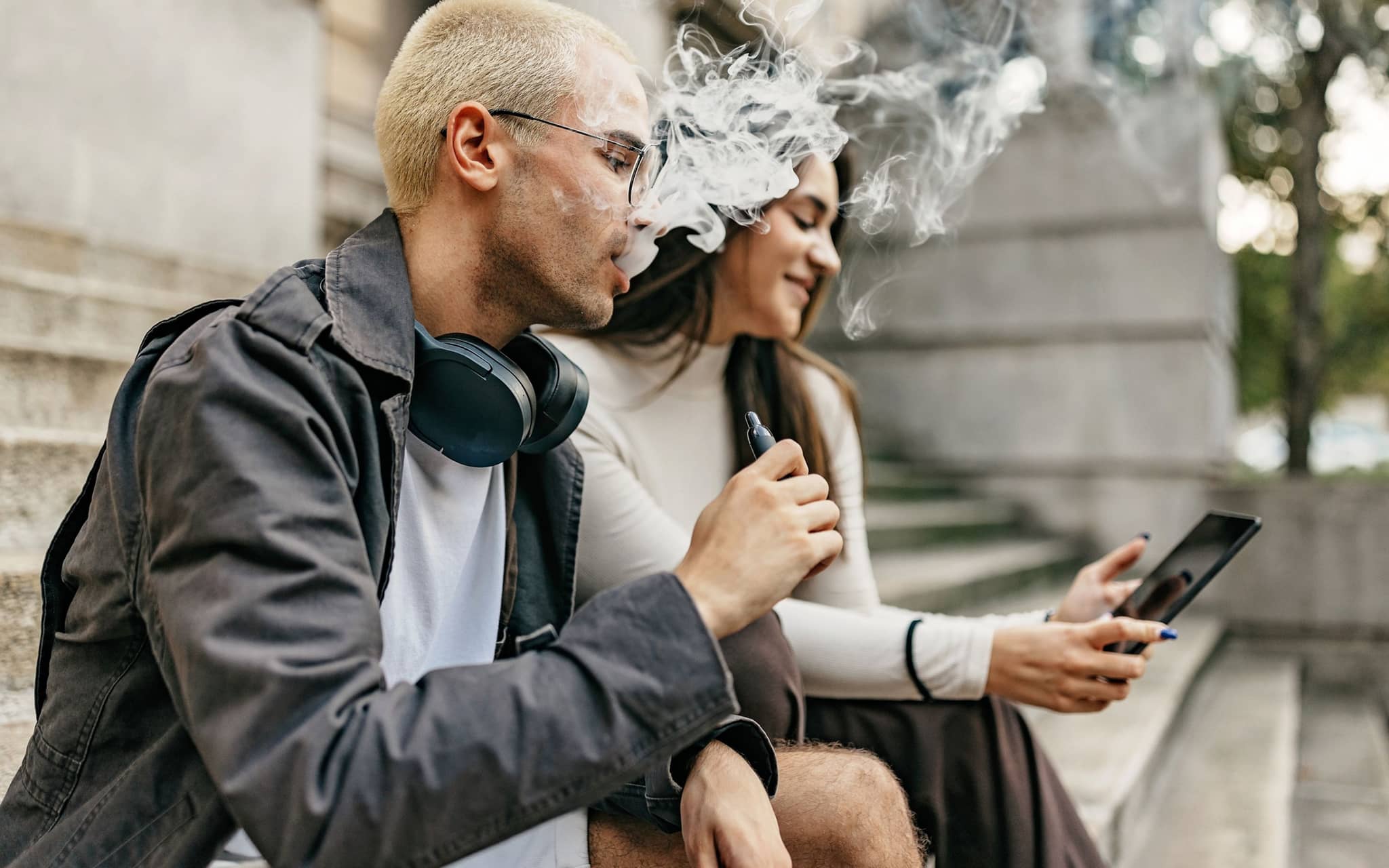 Vapen: Ein junger Mann und eine junge Frau sitzen auf einer Treppe, während der Mann eine E-Zigarette raucht.
