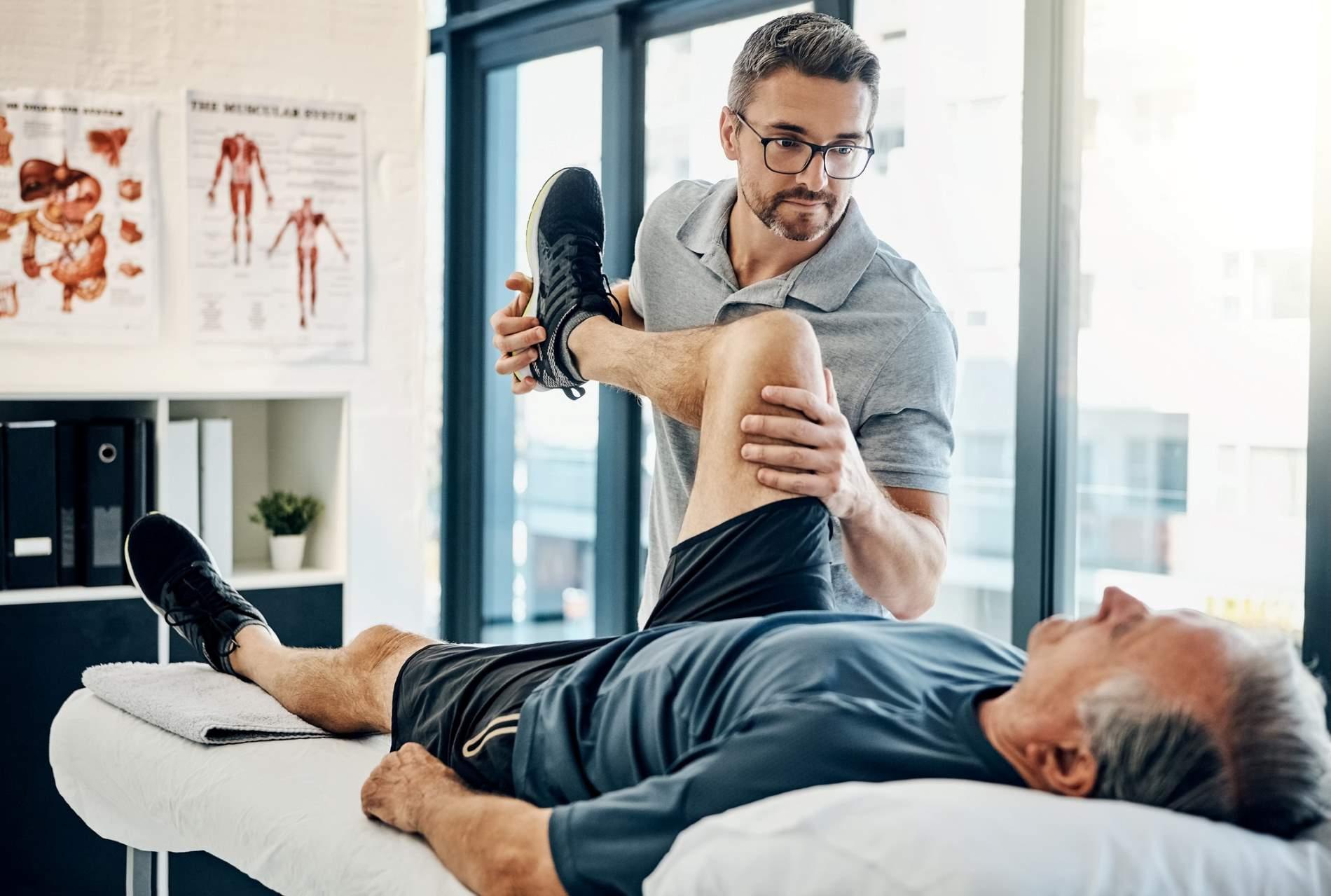 Physiotherapie: Mann behandelt Knie eines Patienten auf einer Liege.