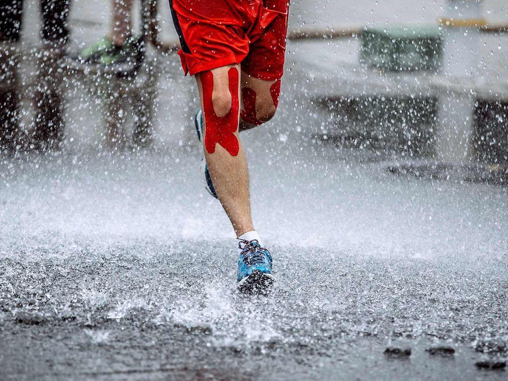 Kinesiotape: Mann mit Kinesiotape am Knie läuft durch Regen.