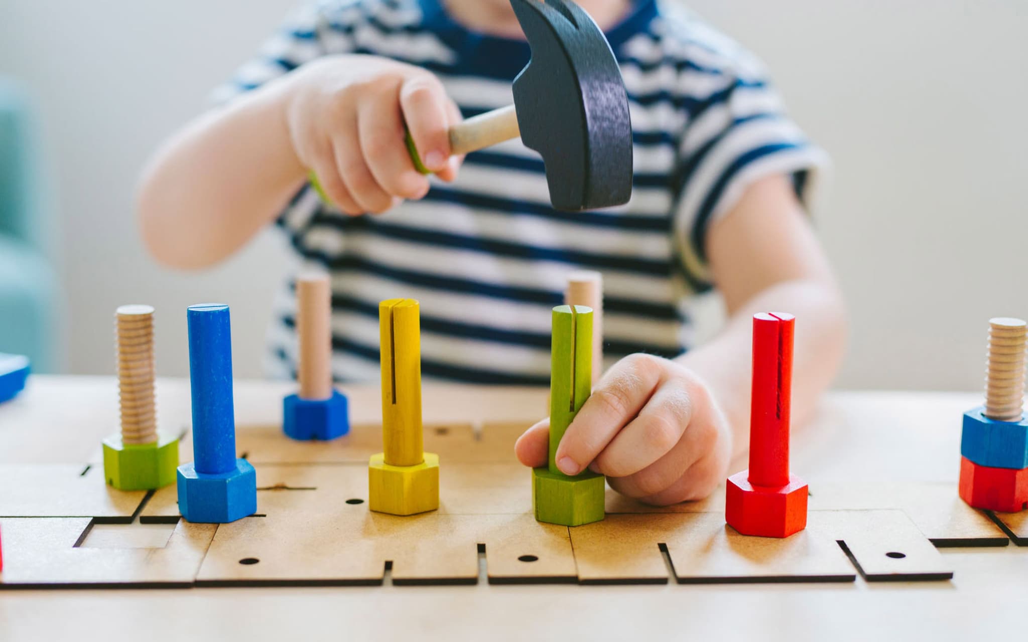 Ergotherapie: Kind schlägt mit Holzhammer auf bunte Holzschrauben.