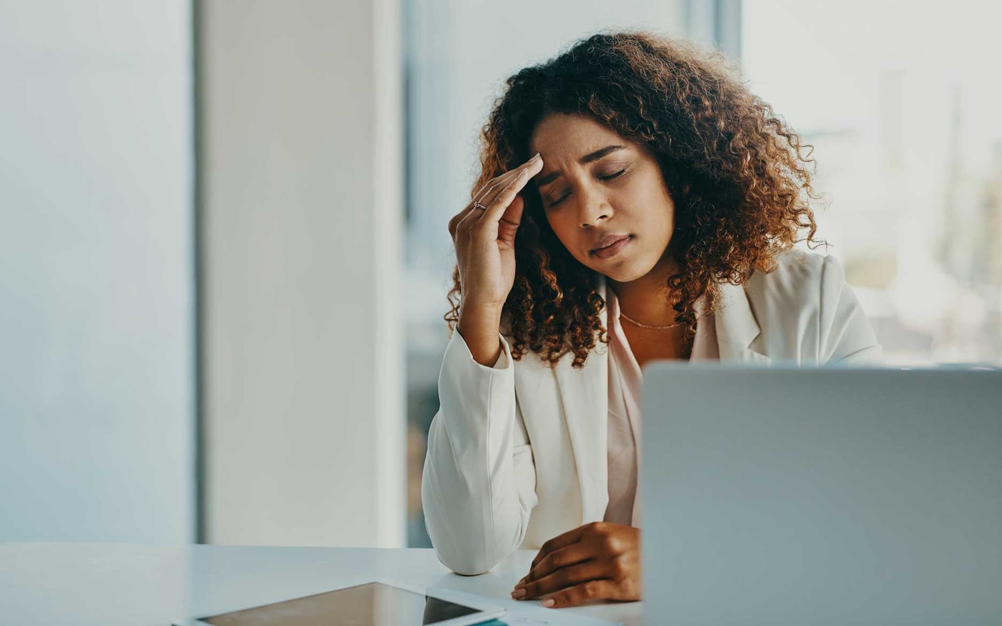 Präsentismus: Junge Frau sitzt am Schreibtisch und fühlt sich unwohl