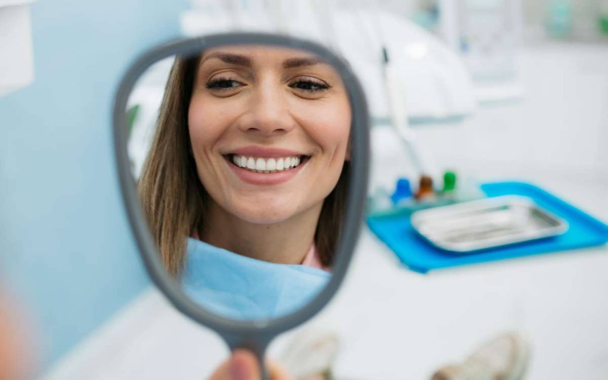 Professionelle Zahnreinigung: Junge Frau schaut sich nach der Behandlung ihre Zähne im Spiegel an.