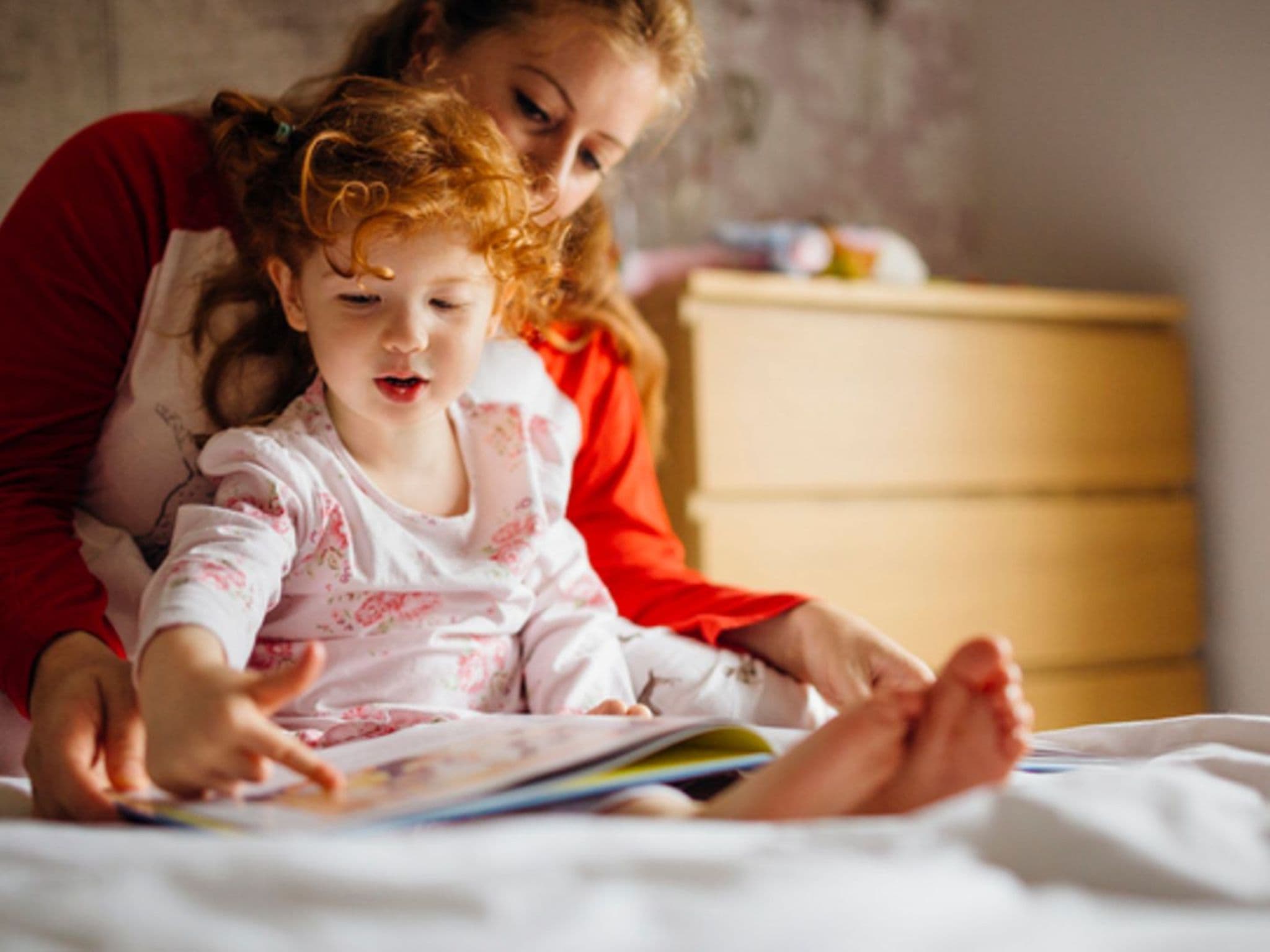 Tagesroutinen: Tochter sitzt im Schoß ihrer Mutter und sie schauen zusammen ein Buch an