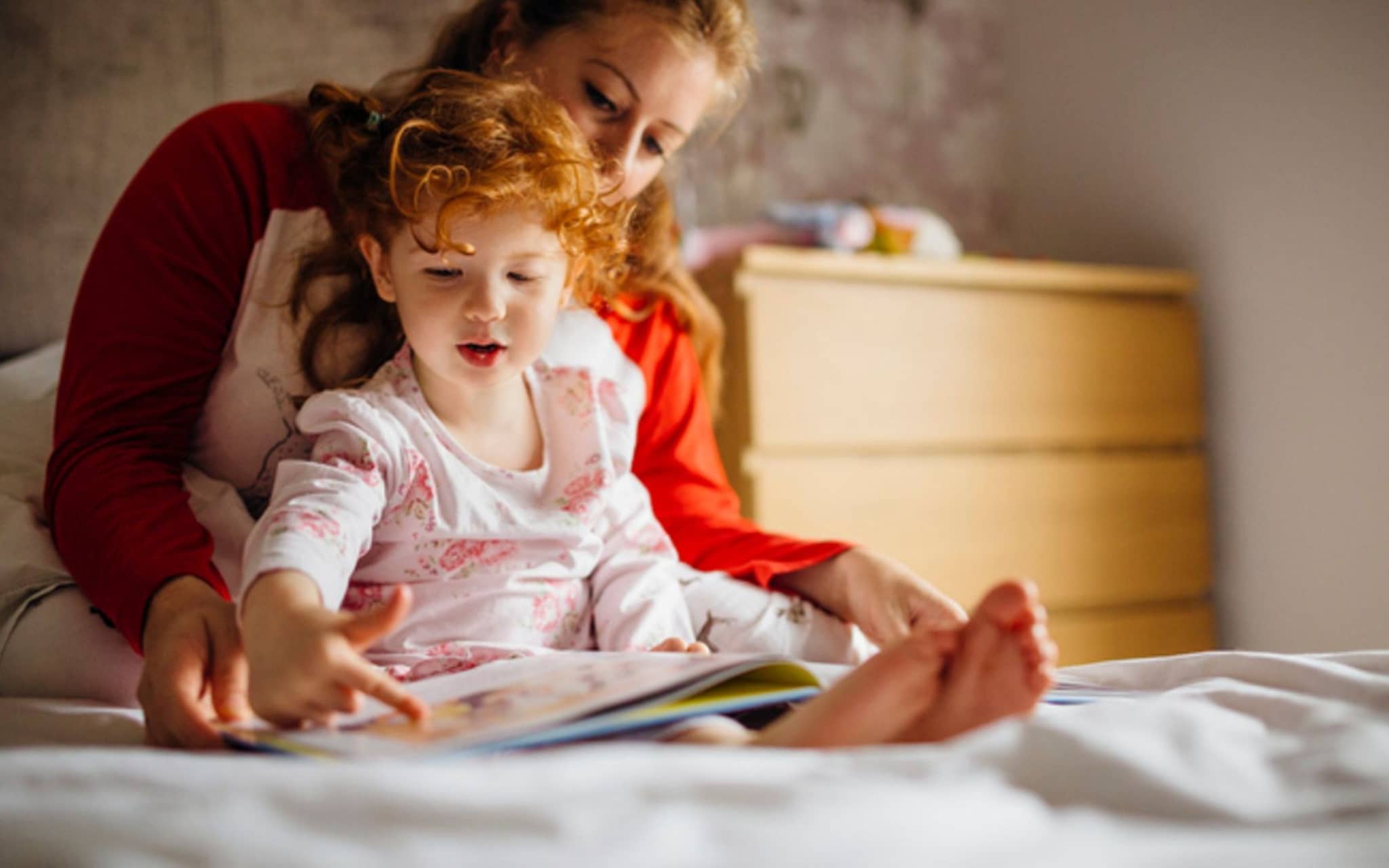 Tagesroutinen: Tochter sitzt im Schoß ihrer Mutter und sie schauen zusammen ein Buch an