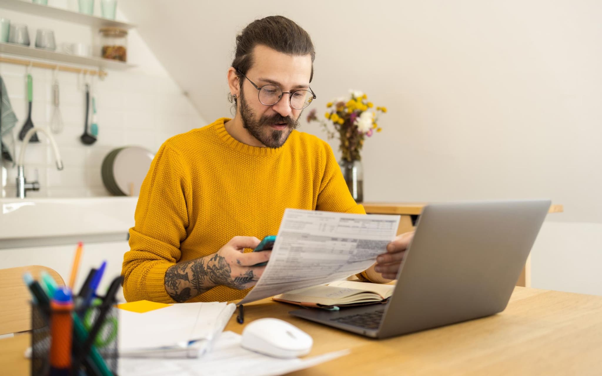 Widersprüche: Ein Mann sitzt in seiner Küche vor einem Notebook und hält ein Anschreiben in der Hand.