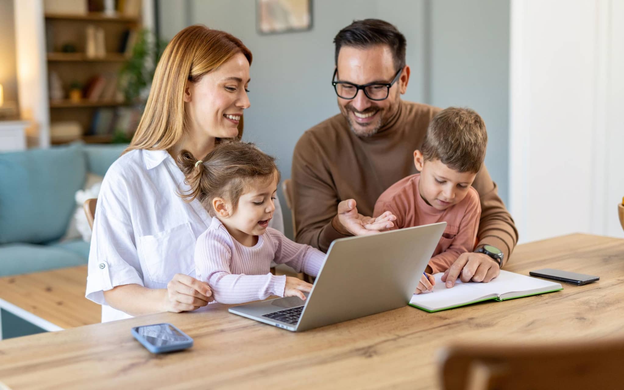 Bonusprogramm: Junge Familie mit zwei Kindern sitzt zuhause gemeinsam vor einem Notebook.