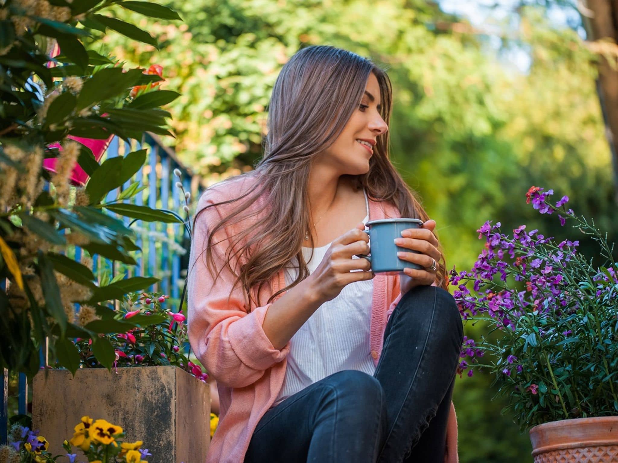 Junge Frau sitzt im Garten und schaut auf ihre Pflanzen. Sie trinkt eine zubereitete Zichorienwurzel als Kaffee-Ersatz.
